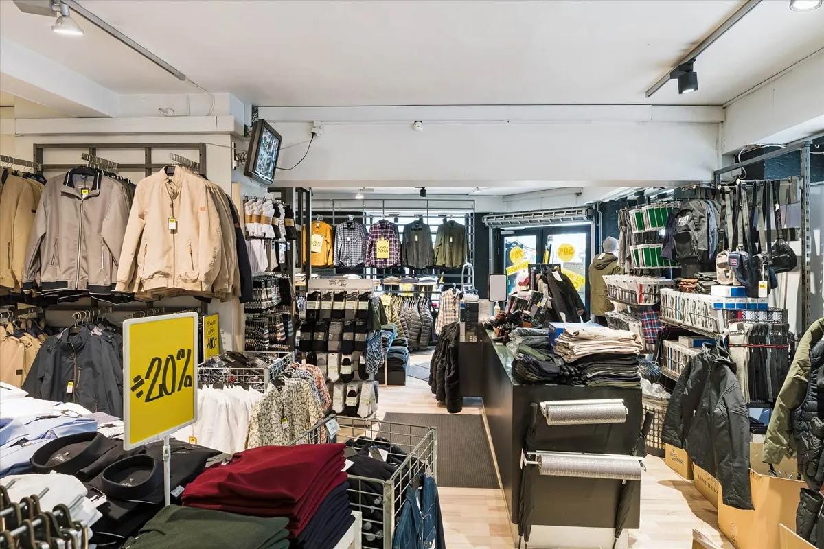 En stor butik med tøj og jakkestativer, indretning med moderne design og tavle med rabat 40% og tv-skærm på væggen