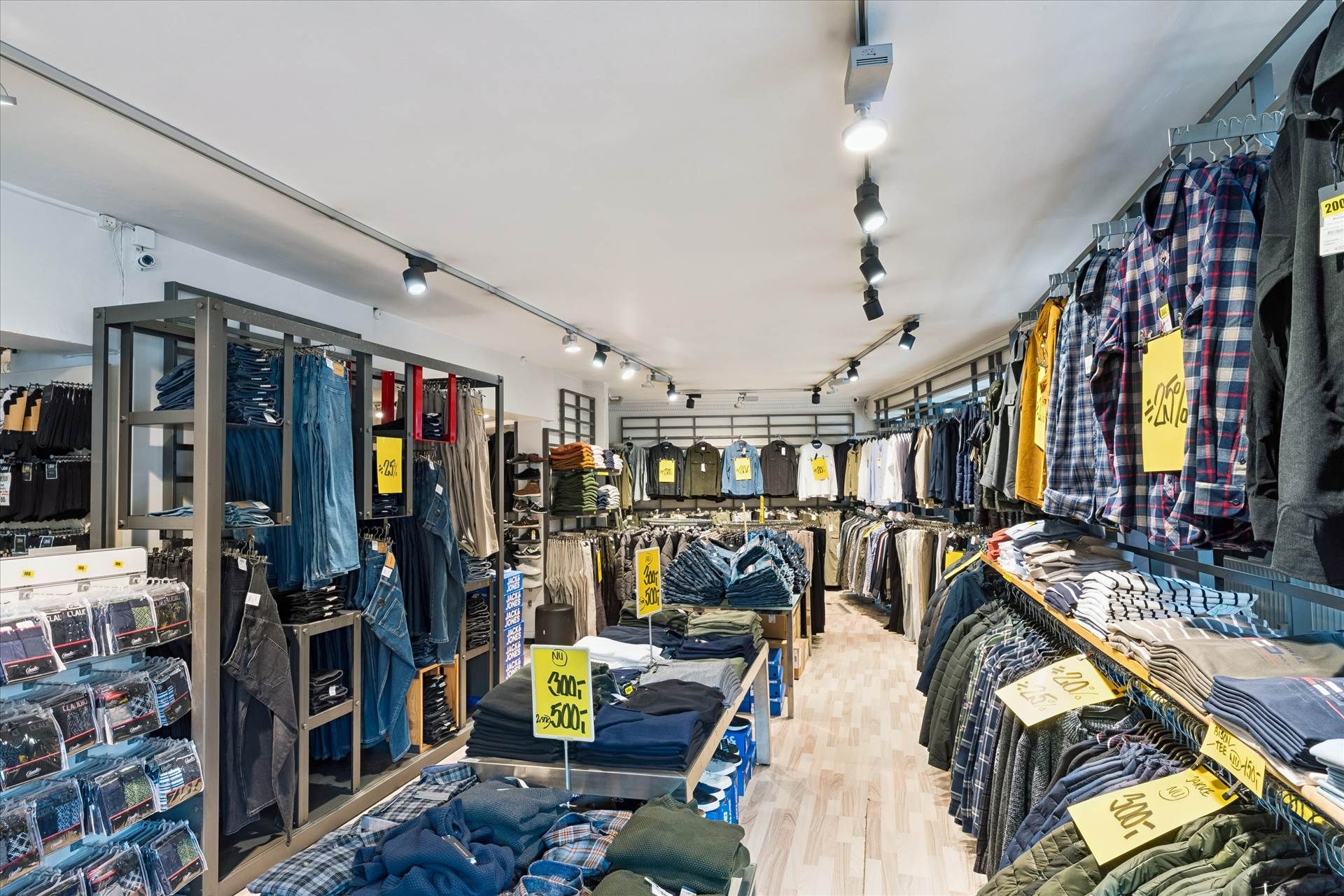 En butik med tøj, undertøj og jeans på hylder, alle med priser, og gulvbelægning i træ