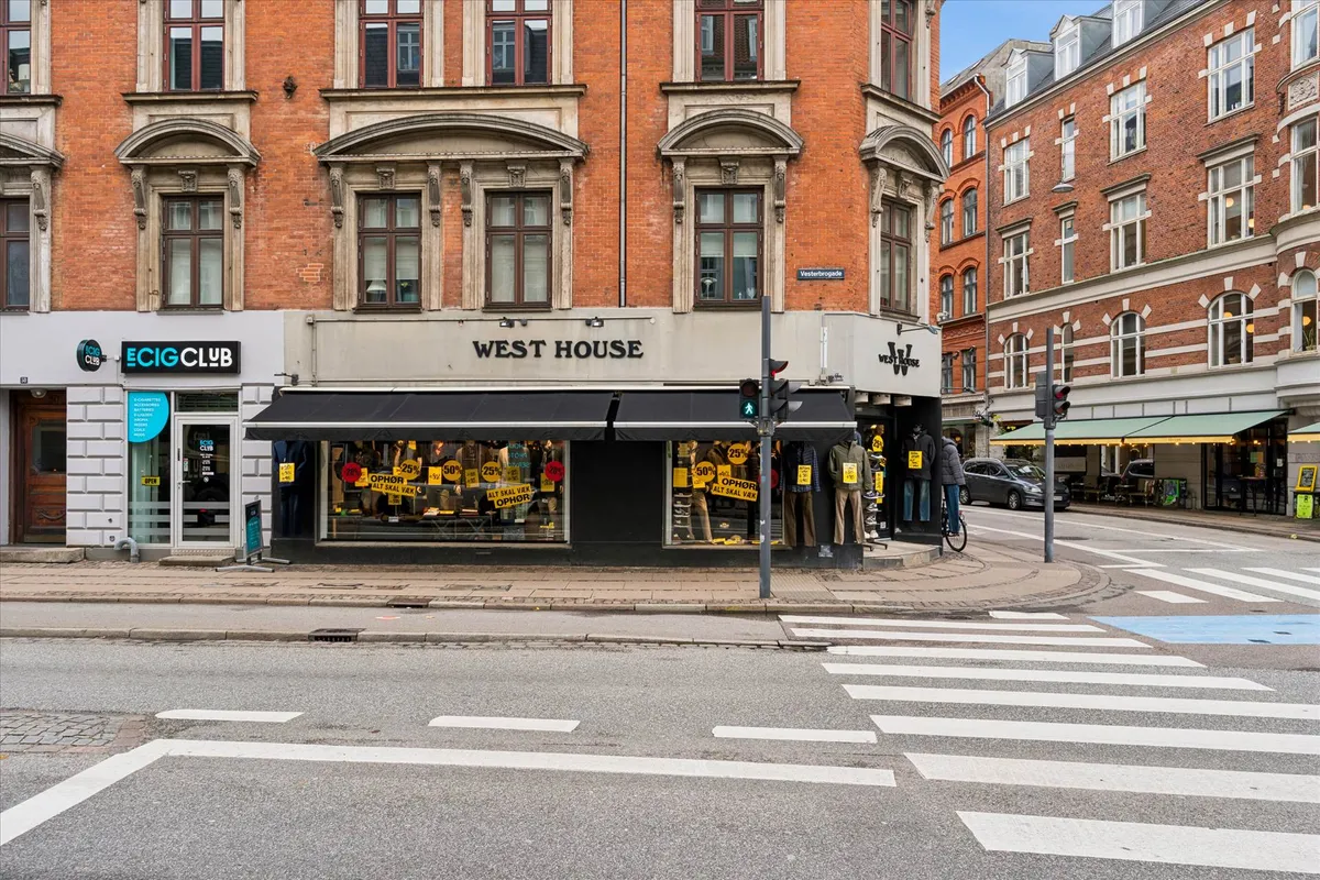 Vesterbro med West House-butik og E-Cig Club-forretning, hvor vejkryds er mærket med hvide streger og en cykel står parkeret