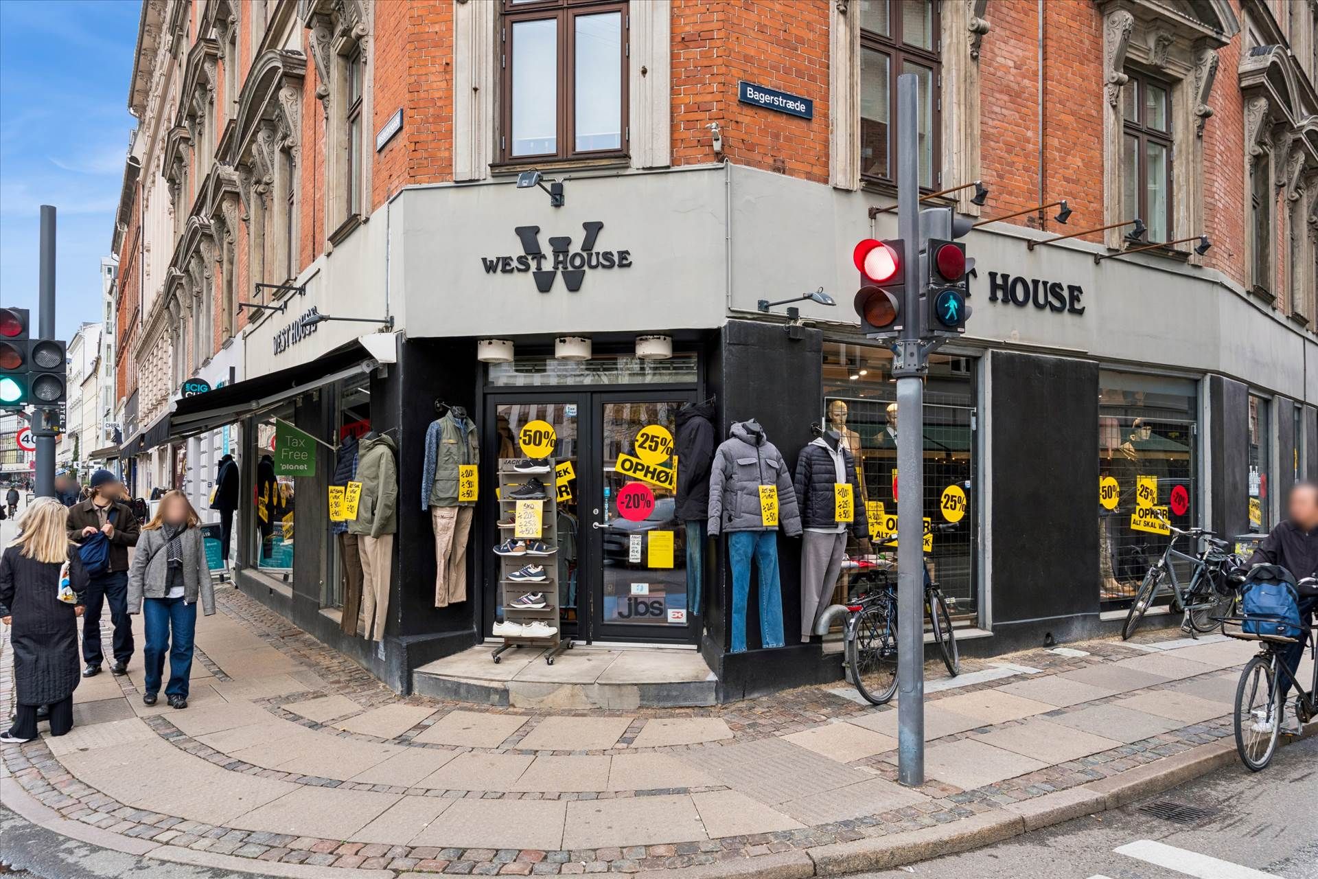 Mennesker går forbi en Westhouse butik på Vesterbro. En cykel med en kuffert er parkeret foran en trafiklys. Butikken har