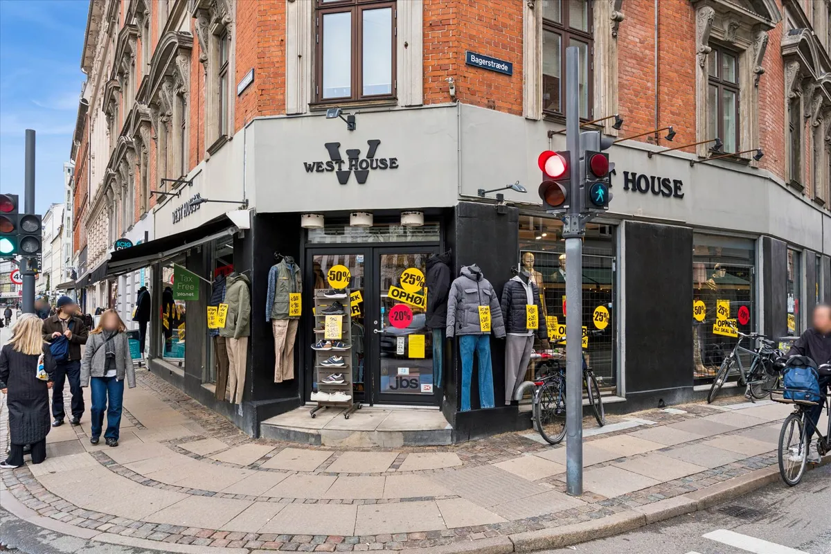 Mennesker går forbi en Westhouse butik på Vesterbro. En cykel med en kuffert er parkeret foran en trafiklys. Butikken har