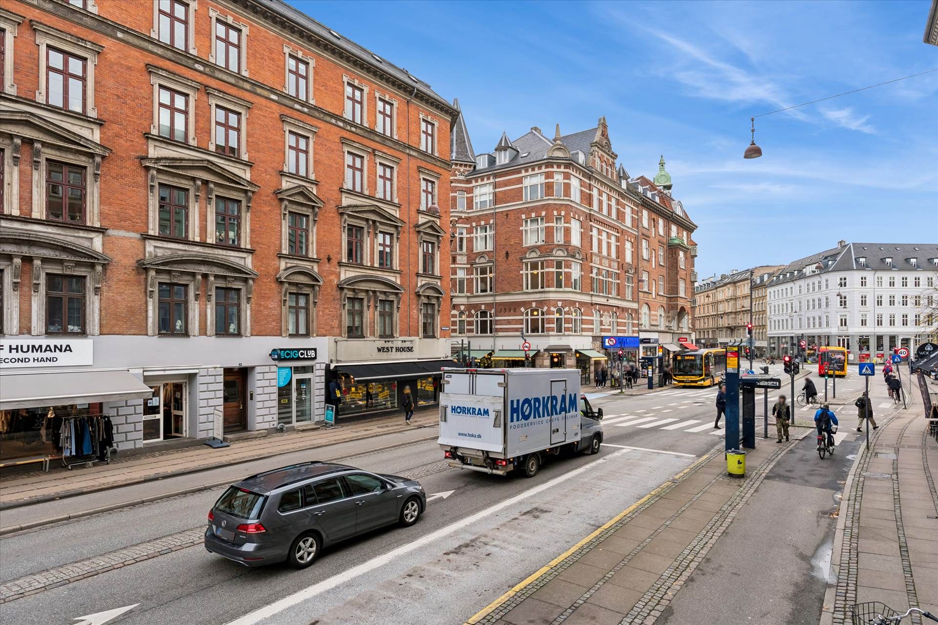 Biler og folk på Vesterbro. En Horkram-vogn og et salgslokal er synlige. Mennesker krydser gaden på fortauet. En bus og et