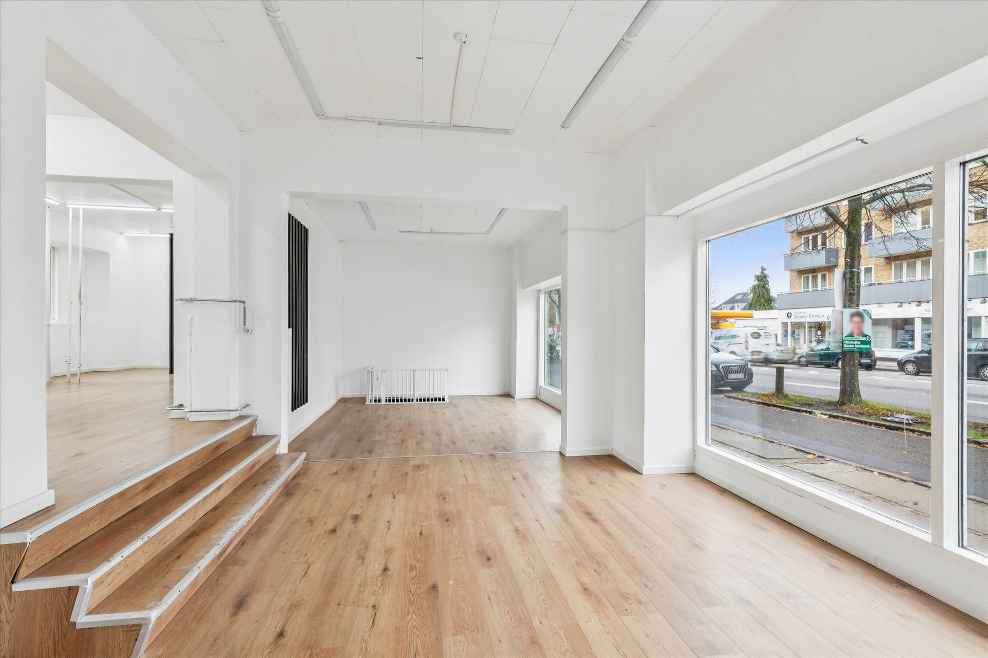 Indvendigt store, lyse ruder, blanke, lysegule trægulve og hvide vægge i en nyrenoveret butik med 93 m²