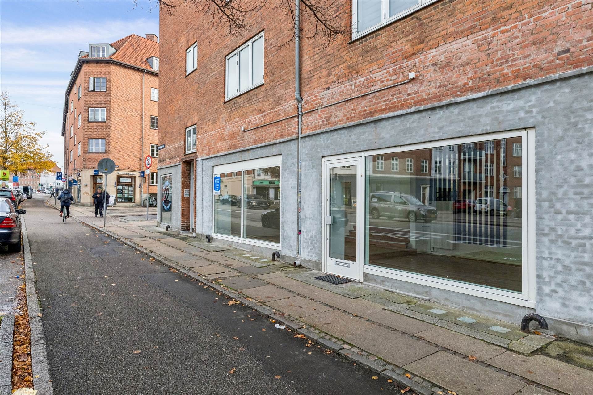 Butikslejemål i Brønshøj med glasfronter og flere biler parkeret på hjørnet af gaden