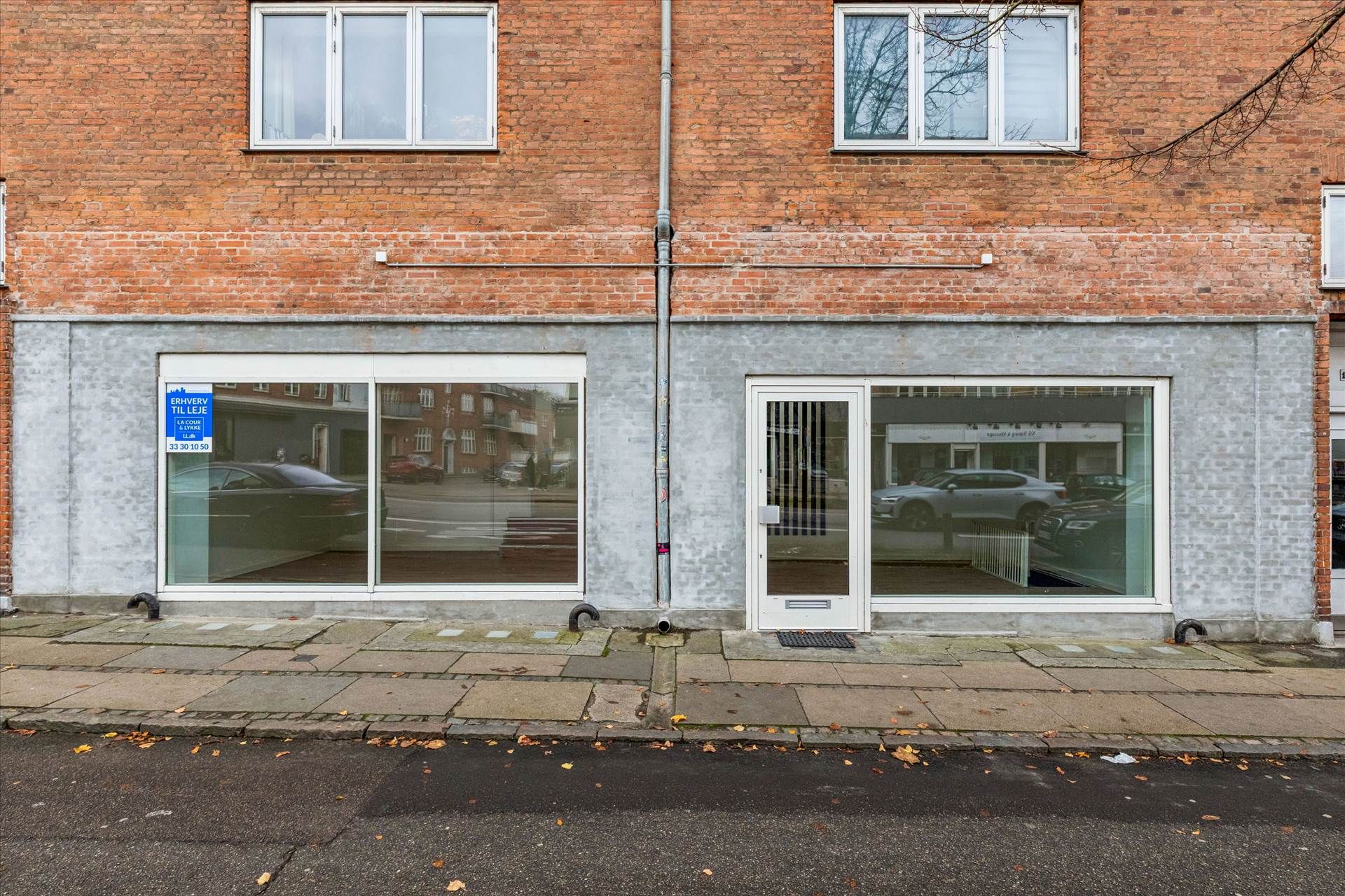 Store glasruder og hvide døre på en rødmalet bygning i Brønshøj med røde mursten og to etager med vinduer