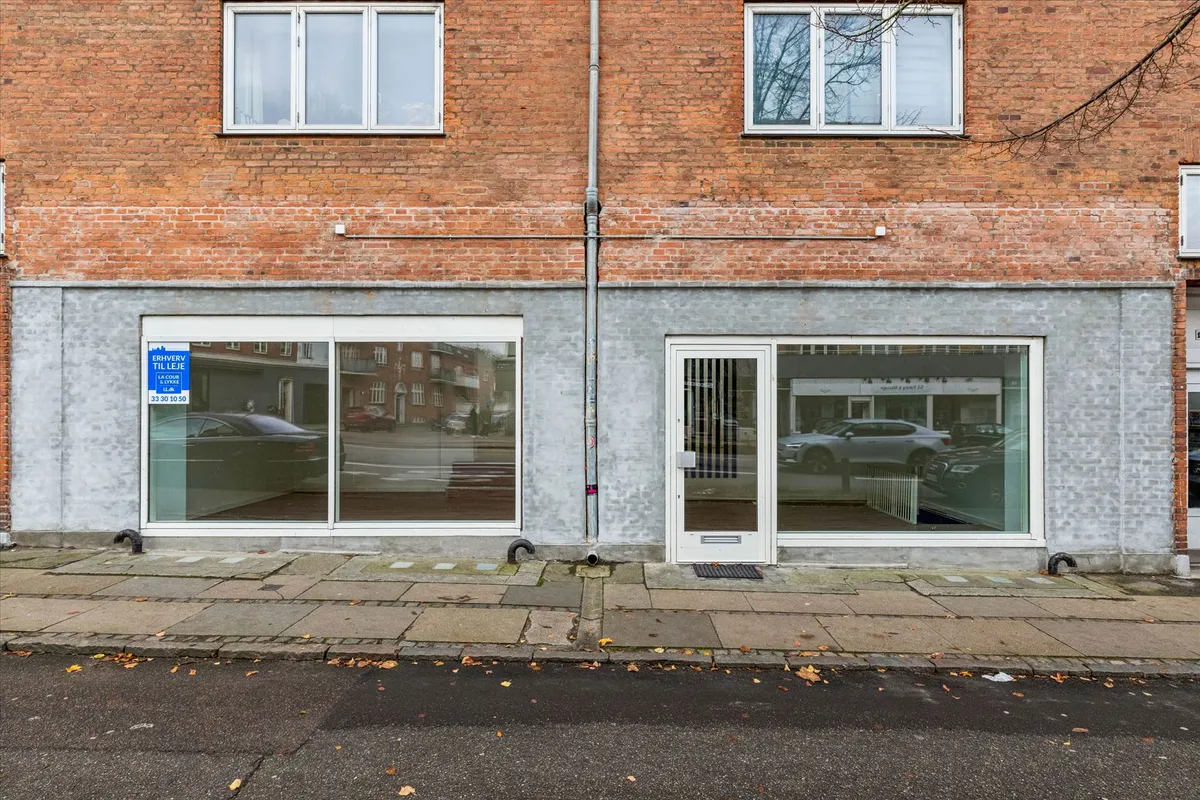 Store glasruder og hvide døre på en rødmalet bygning i Brønshøj med røde mursten og to etager med vinduer