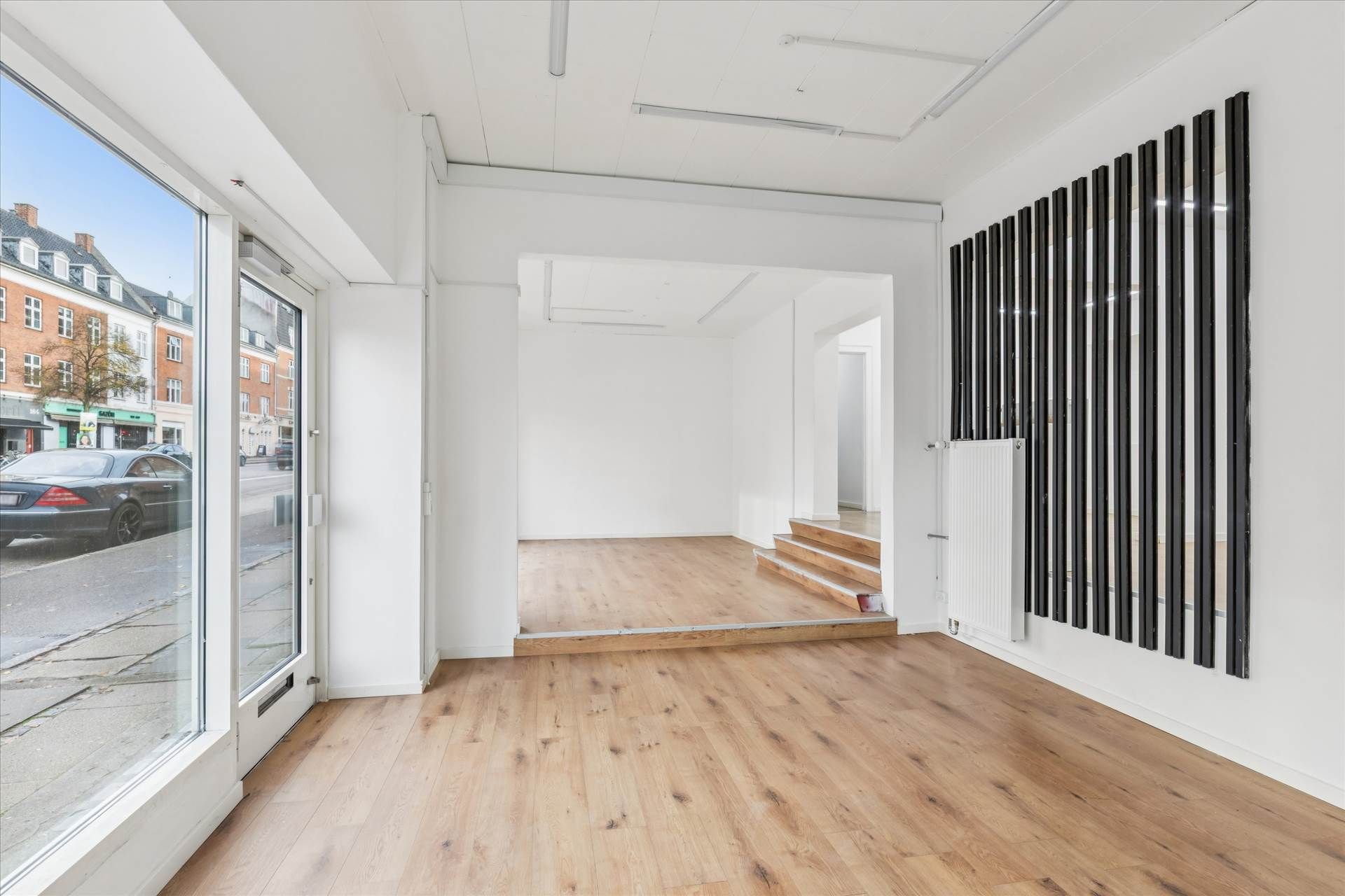 En stor, lys og rummelig butik med trægulv og hvide vægge, store vinduer og en trappe op til et loft