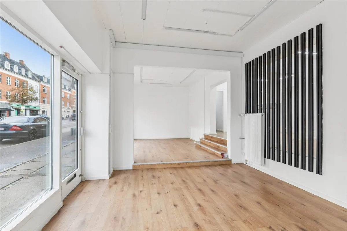 En stor, lys og rummelig butik med trægulv og hvide vægge, store vinduer og en trappe op til et loft