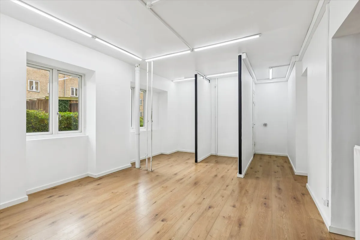 Inde i en stor, tom og ren butikslokaler med hvide vægge, lyse gulvbelægning og slanke, sorte hjørner og søjler.