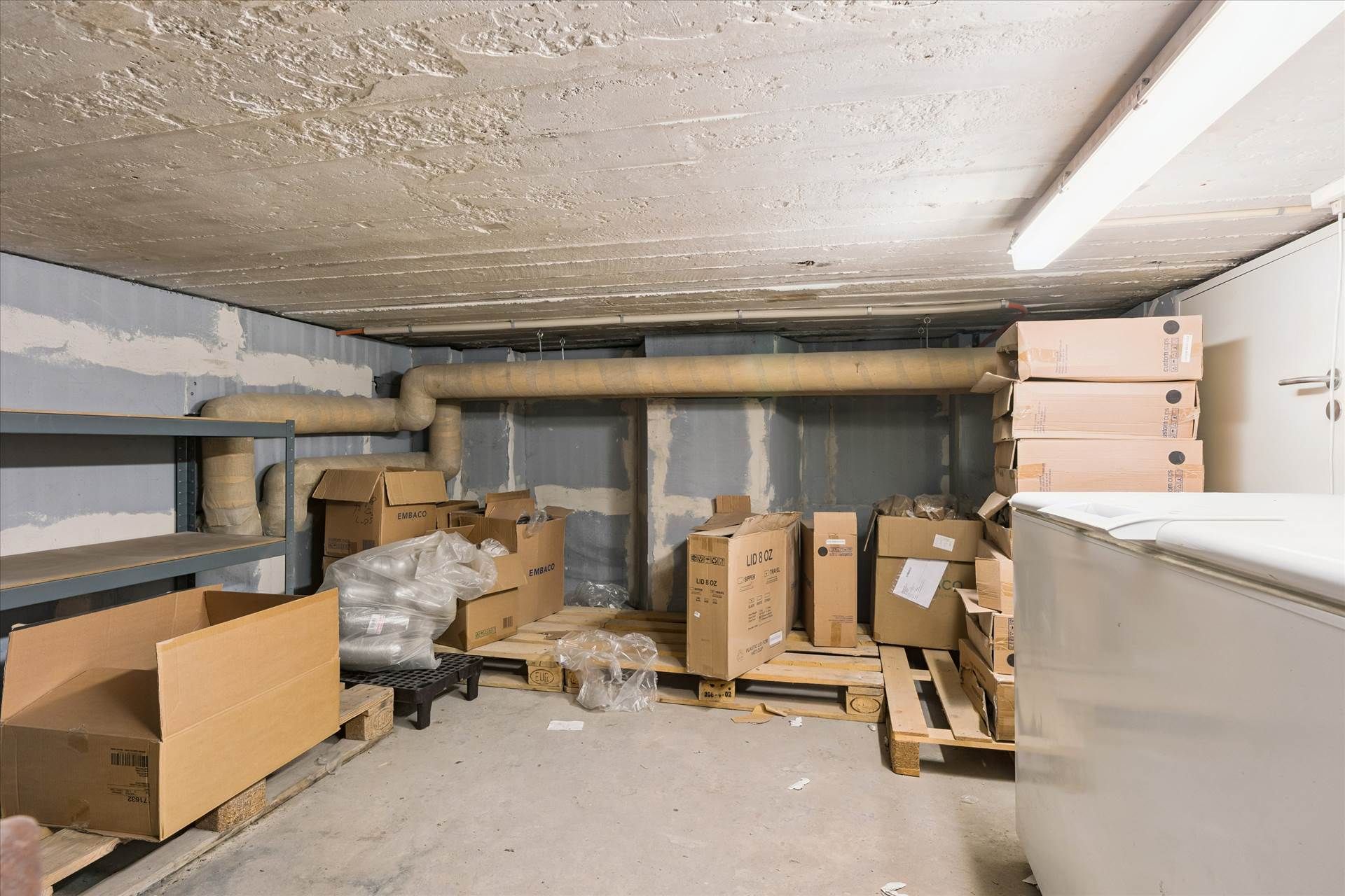 En lagerlokale med flere kasser, emballage og ventiler på væggen samt en køleskab og et lagerreol