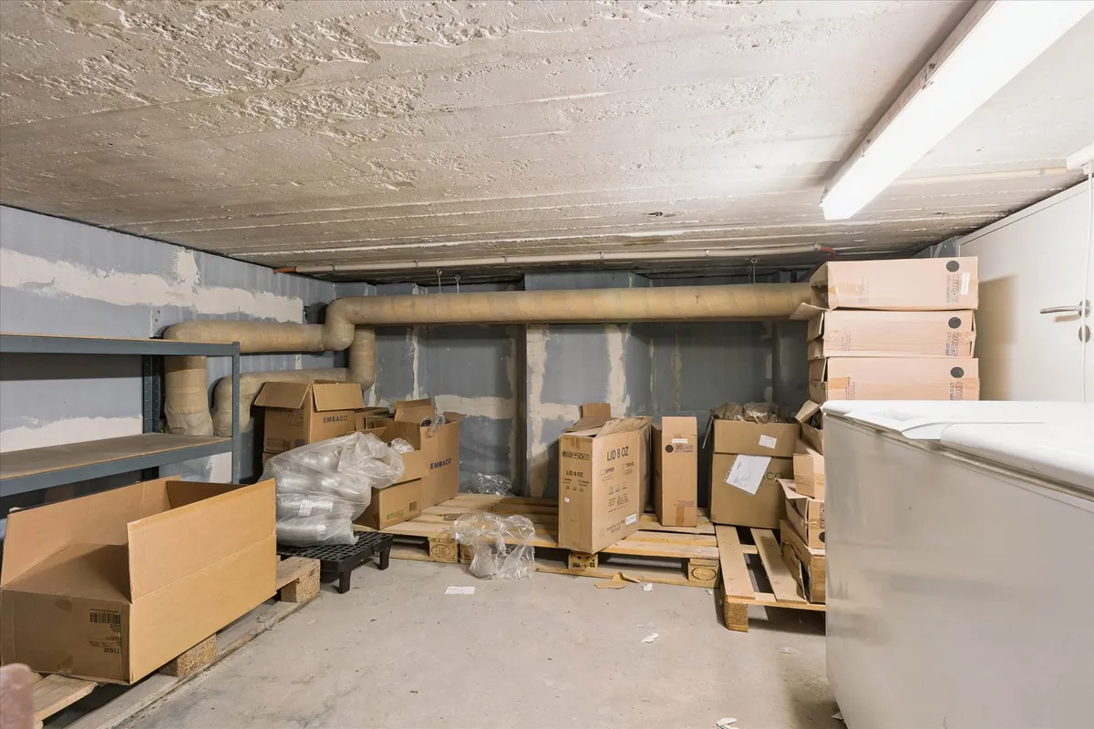 En lagerlokale med flere kasser, emballage og ventiler på væggen samt en køleskab og et lagerreol