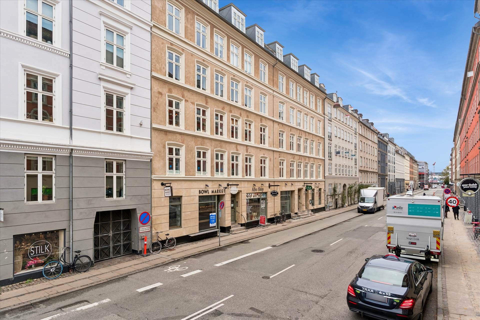 En bil og en lastvogn kører ad en gade med et lokale med udsalgsskiltet Stilk Copenhagen.