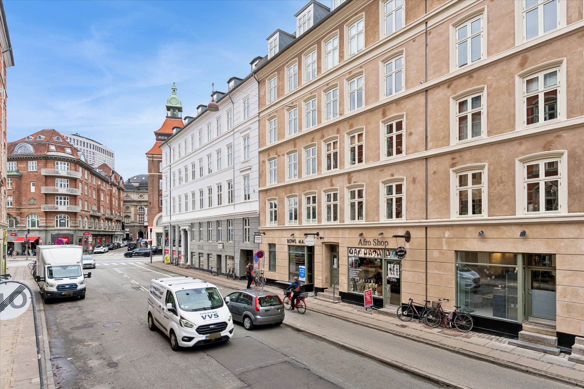 Vej med biler og cykler, forretninger og bygninger, sammen med folk og udsigt til en bygning med en røgdom og en grøn kuppel