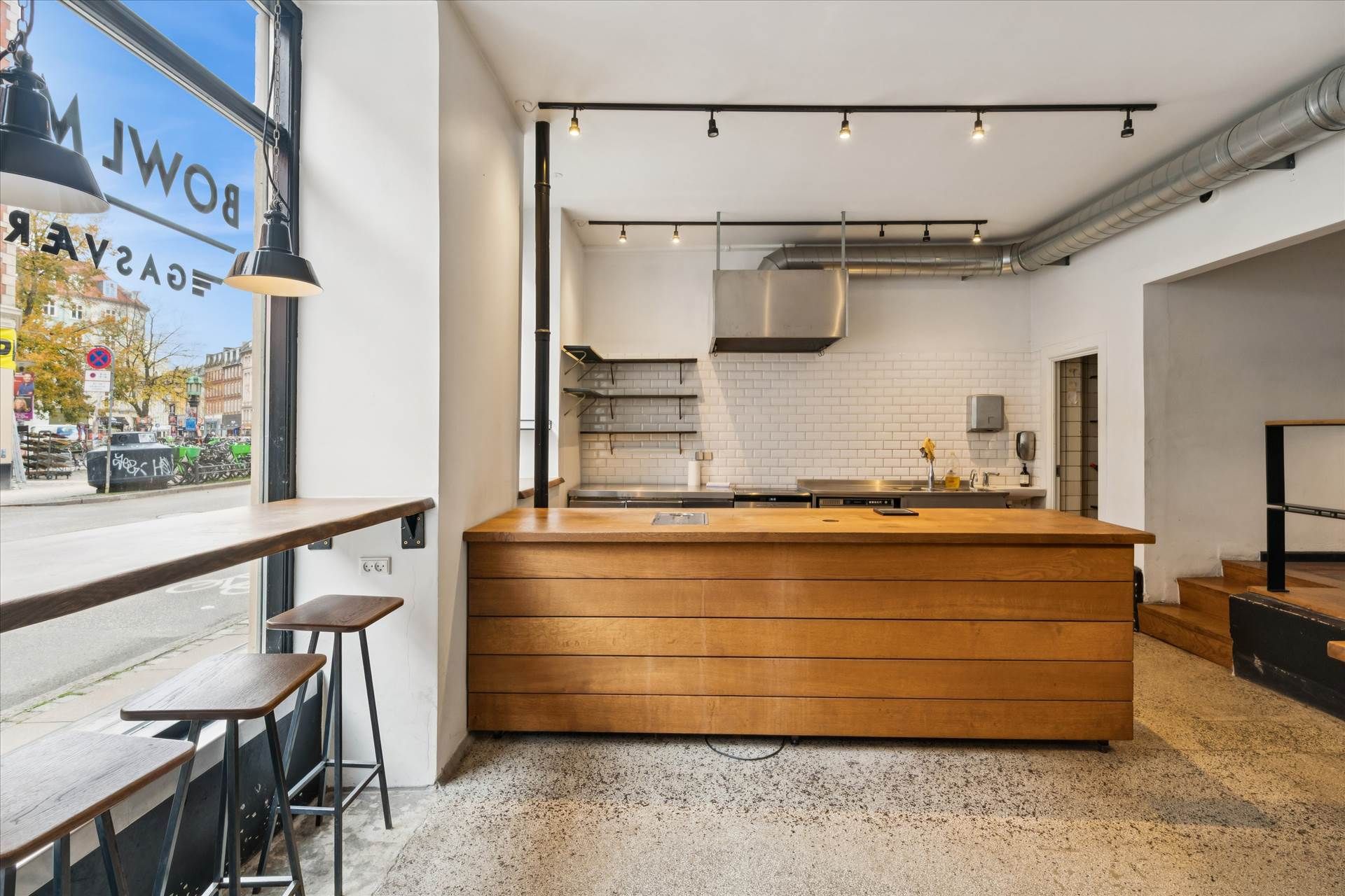 Køkken med massivt træ bord, lysekroner, høje stole og lyse blyantlamper samt køkkenudstyr og en stor vinduesfront