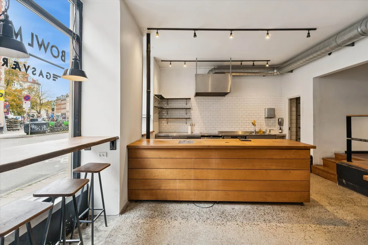 Køkken med massivt træ bord, lysekroner, høje stole og lyse blyantlamper samt køkkenudstyr og en stor vinduesfront