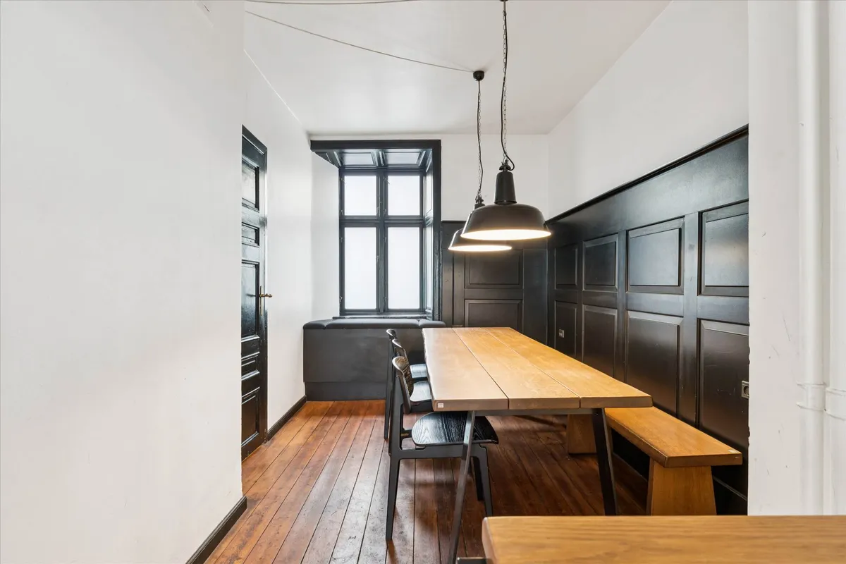 Værelse med trægulv og møbler samt vindue med persienner og lysekroner