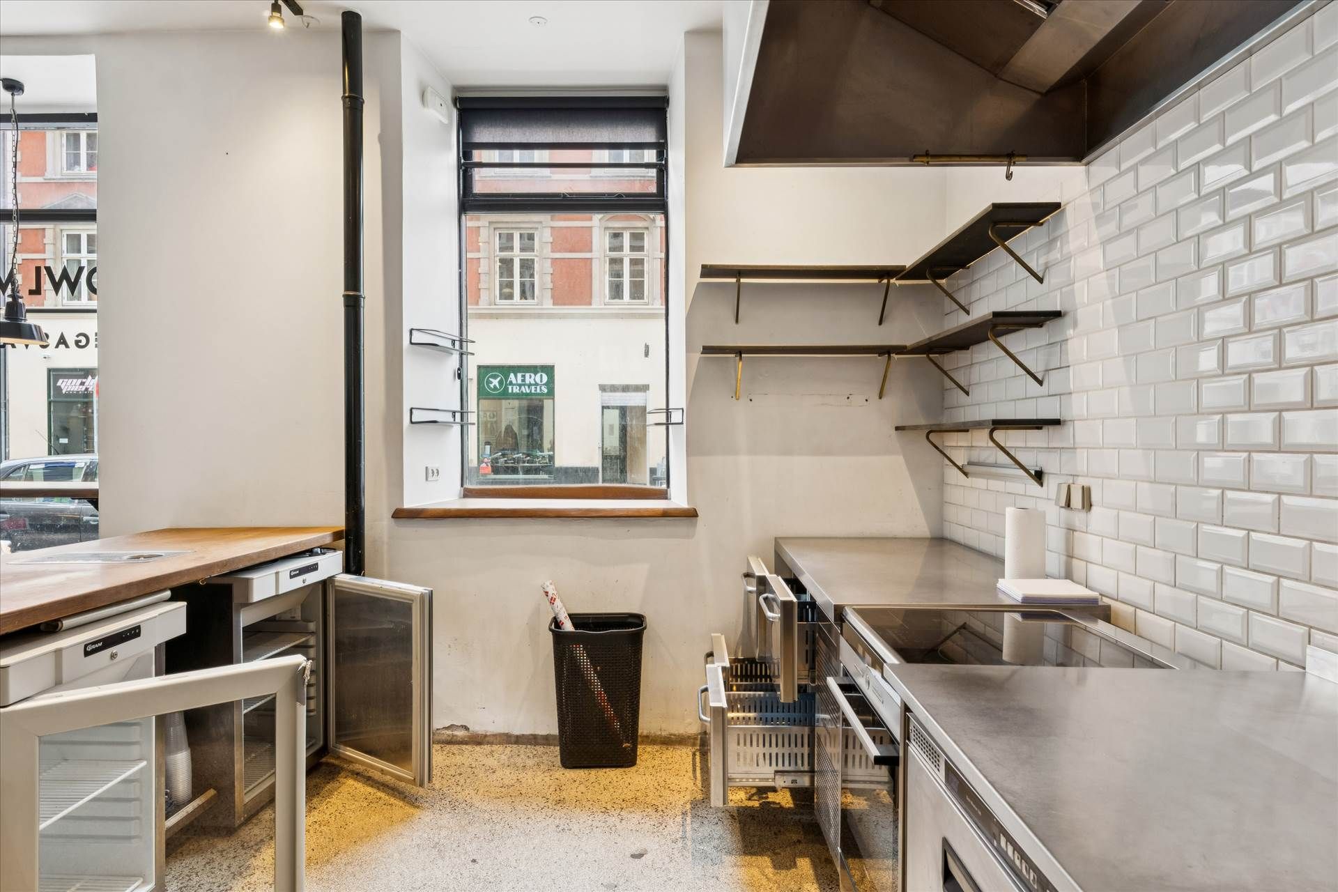 Moderne køkken med lyse krydsfinergulve og rustfrit stålapparater, vinduesglas og stålhylder, åbne køleskabe og