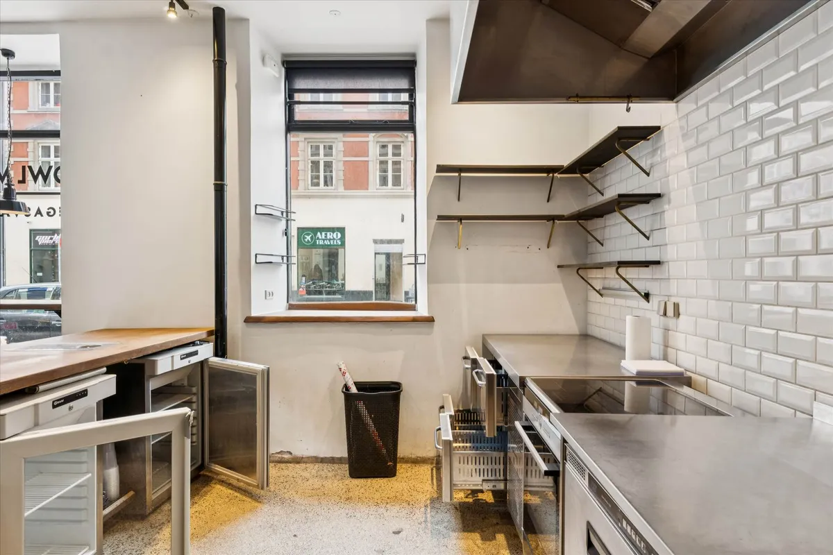 Moderne køkken med lyse krydsfinergulve og rustfrit stålapparater, vinduesglas og stålhylder, åbne køleskabe og