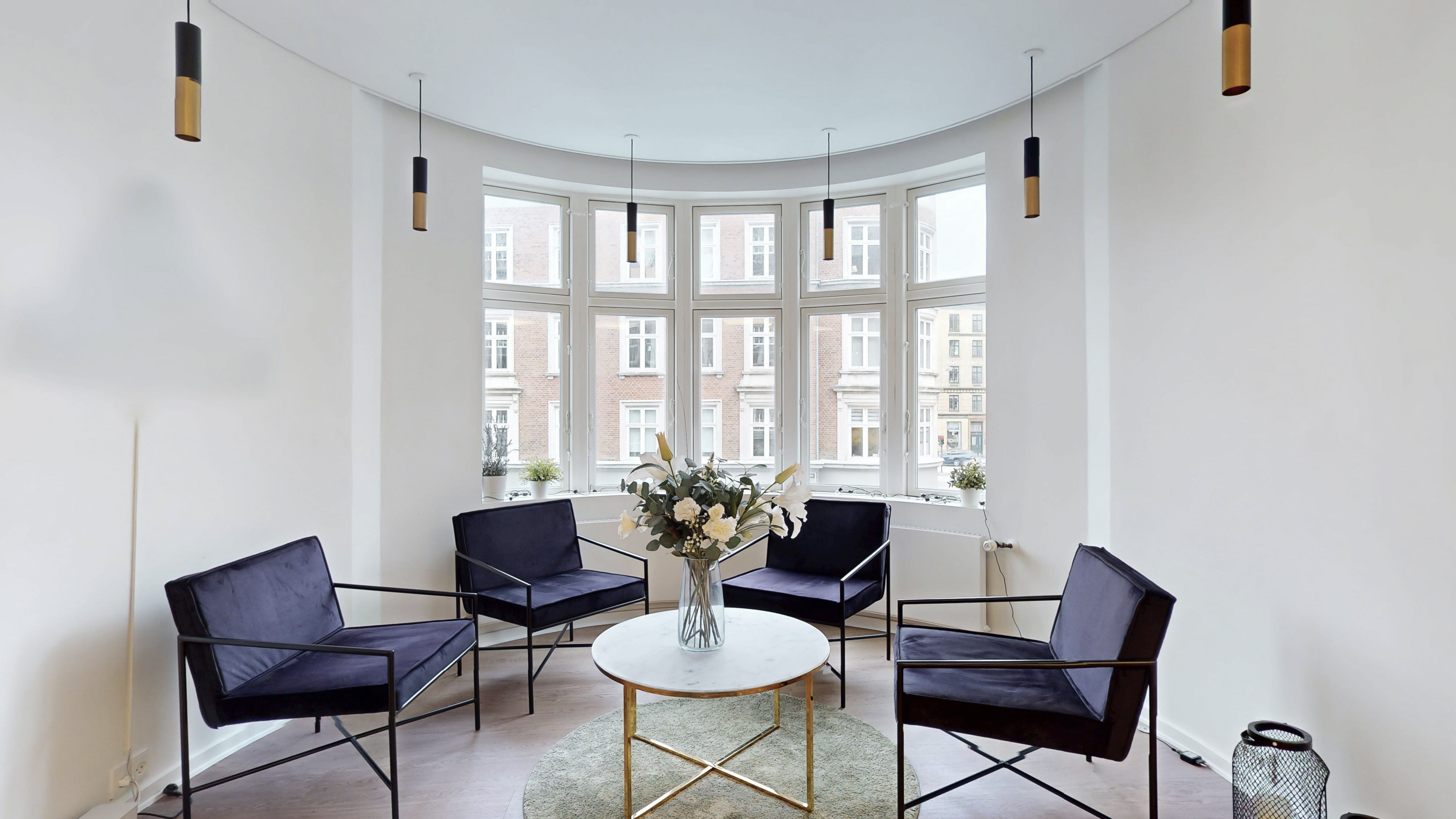 En velholdt lyse stue med runde møbler og hvide vægge samt en rund gulvvand. En hvid rund bord med guldfarvede ben står på