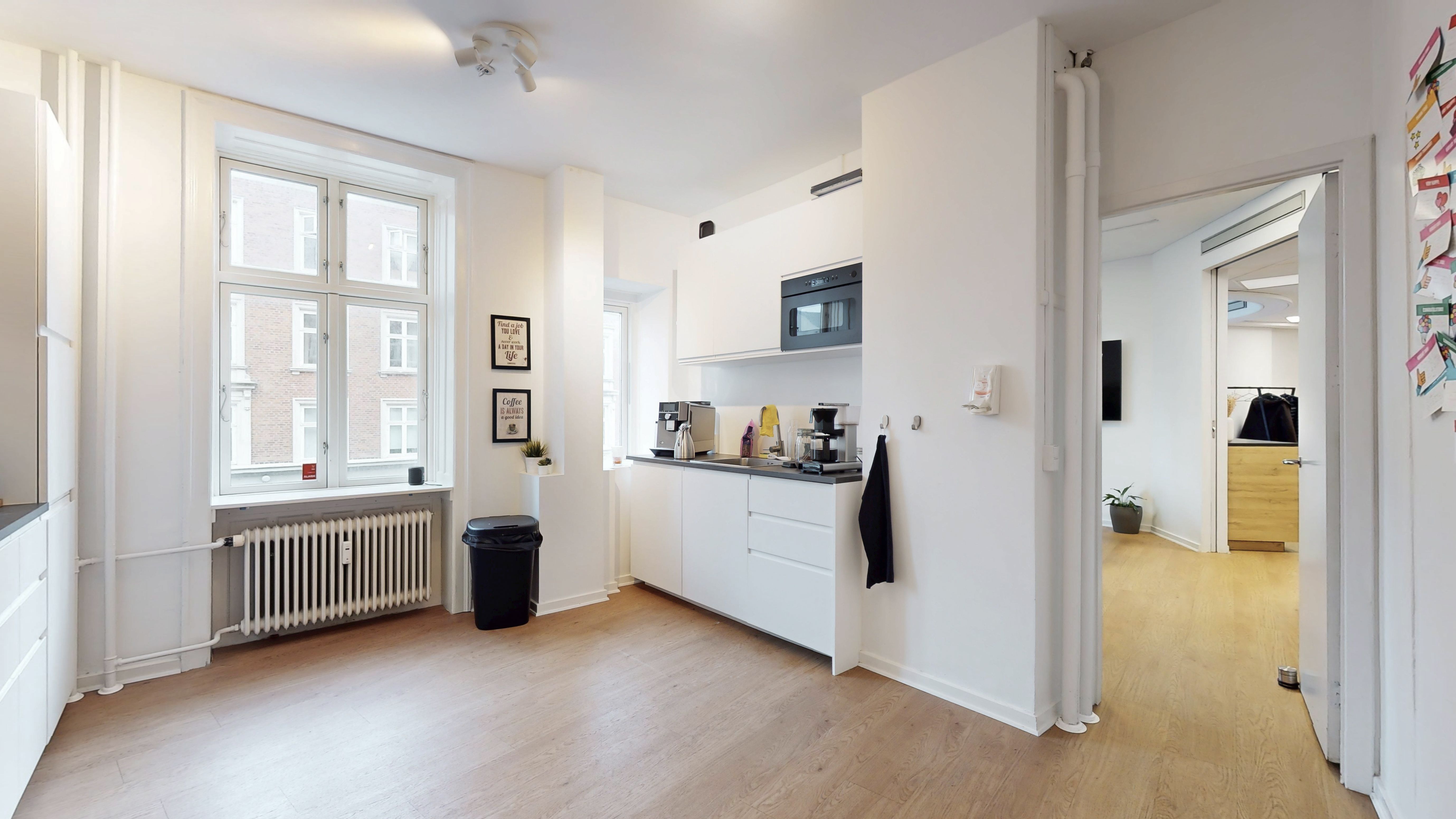 Moderne køkken med hvide vægge og lyse trægulve, underskrevet af minimalistisk design med en mikrobølgeovn og kaffemaskine