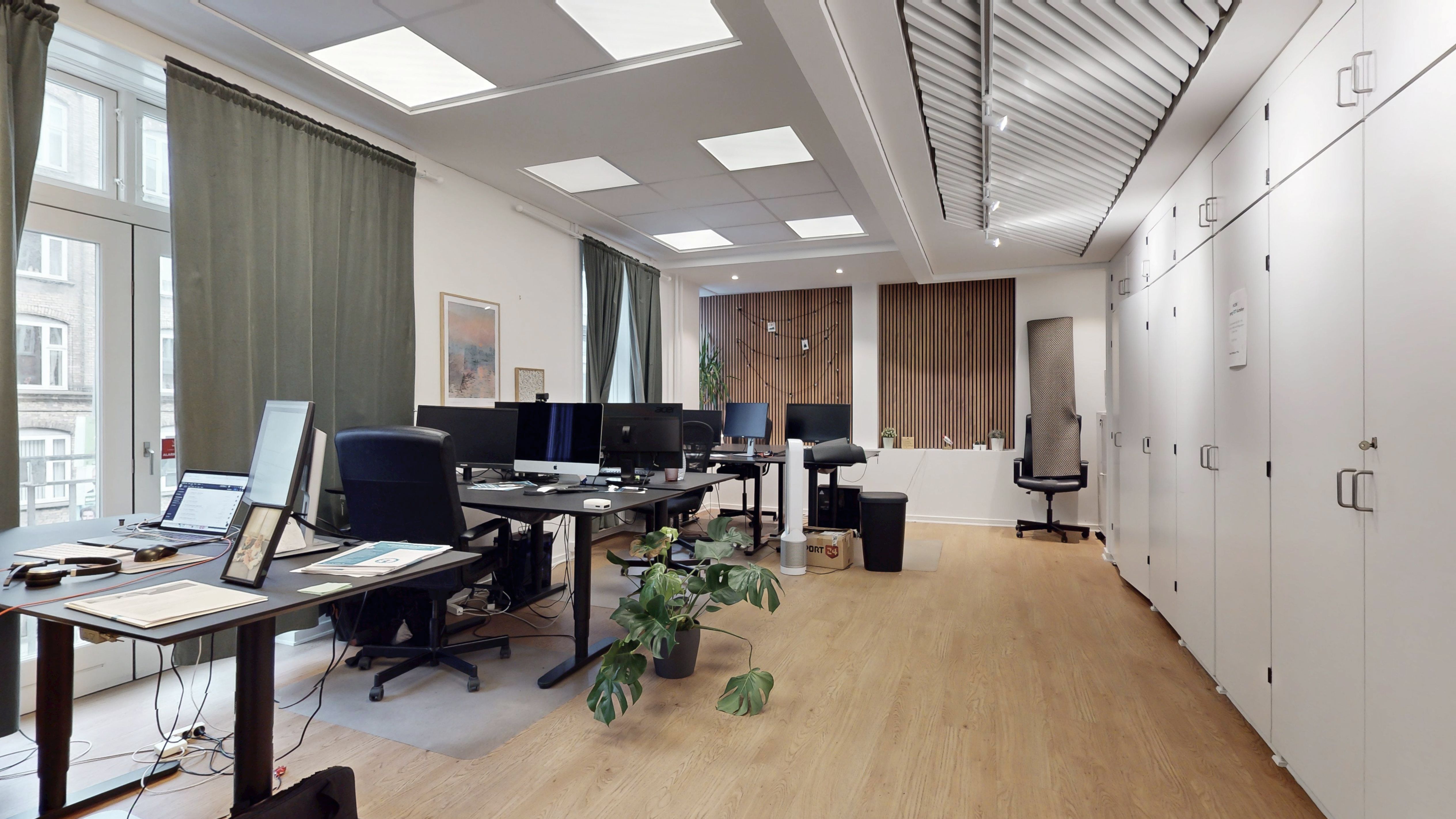 Kontor med flere arbejdsborde og stole samt plante og lysekroner i loftet