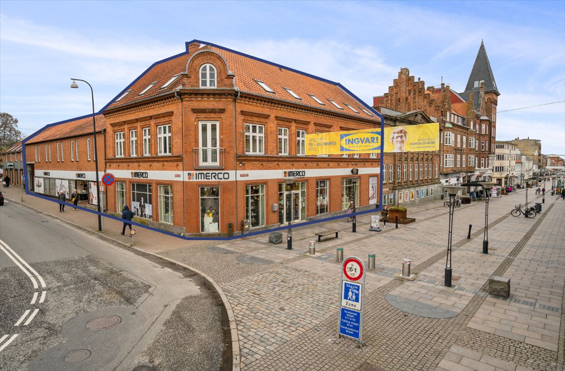 Forretningsbygning med reklamebanner og udsalgsvinduer med teksten "INGVAR!" og "MERCO" samt folk, der går på fortovet
