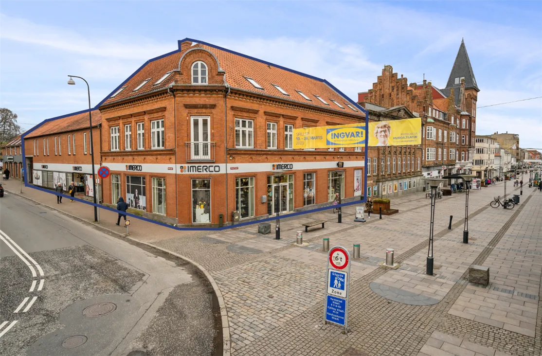 Forretningsbygning med reklamebanner og udsalgsvinduer med teksten "INGVAR!" og "MERCO" samt folk, der går på fortovet