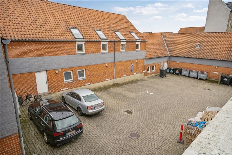 To biler er parkeret på en garageparkeringsplads med røde murstensbygninger og mange vinduer