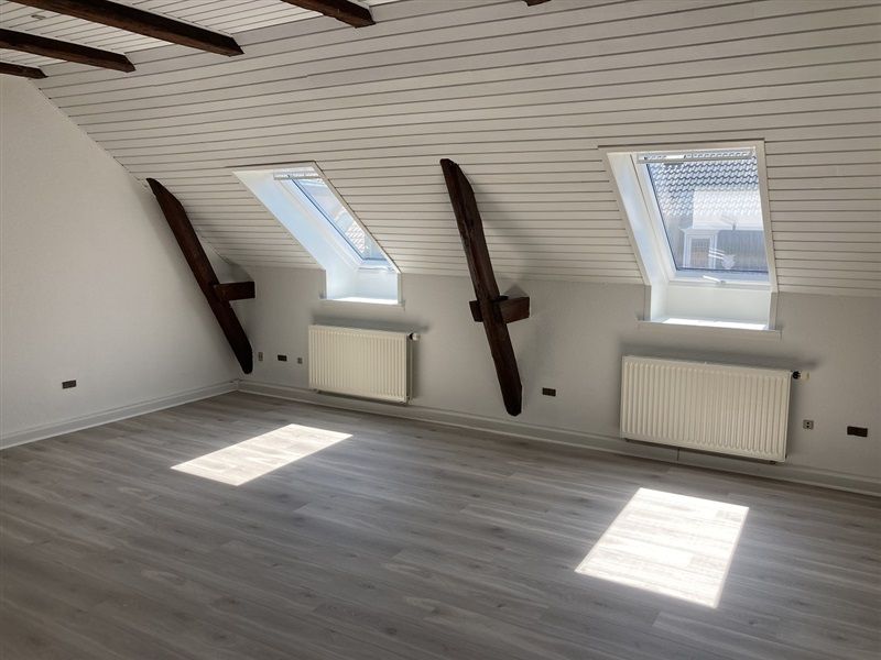 En rummelig loftsværelse med højt til loftet og to store vindue med udgang til en terrasse