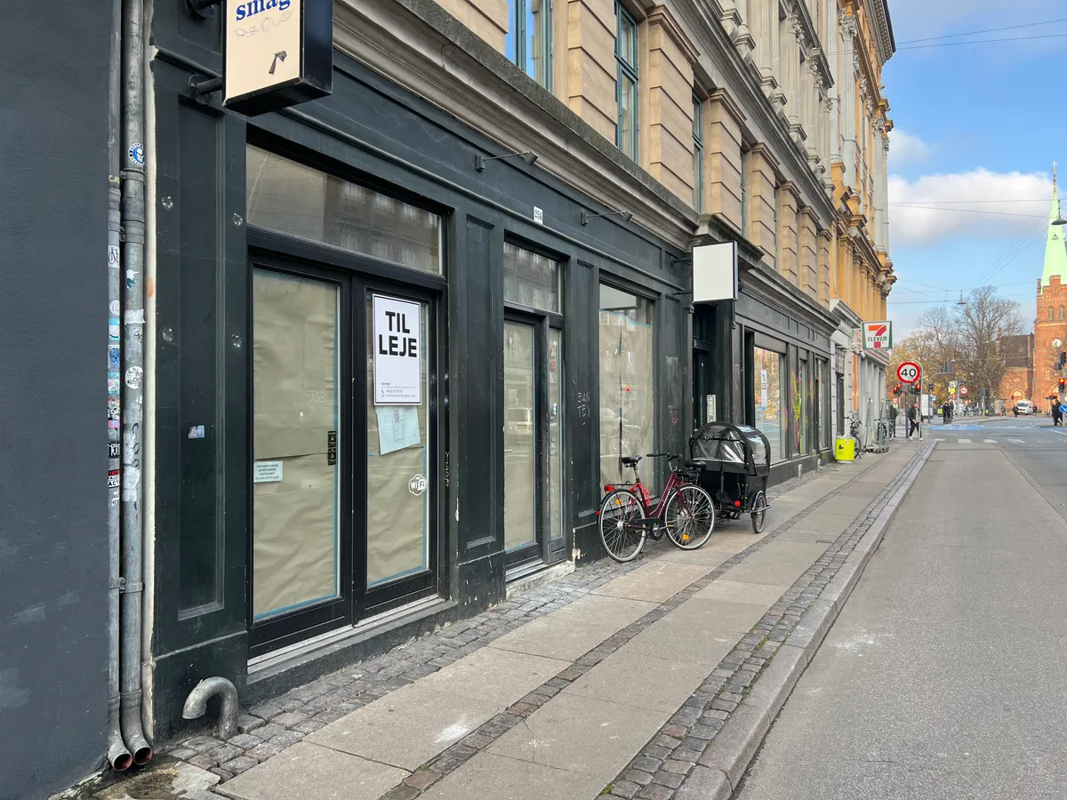 Stænket butikstilbud på Fælledvej 21A med to cykler og en vogn parkeret foran og skilt med teksten "Til Leje"