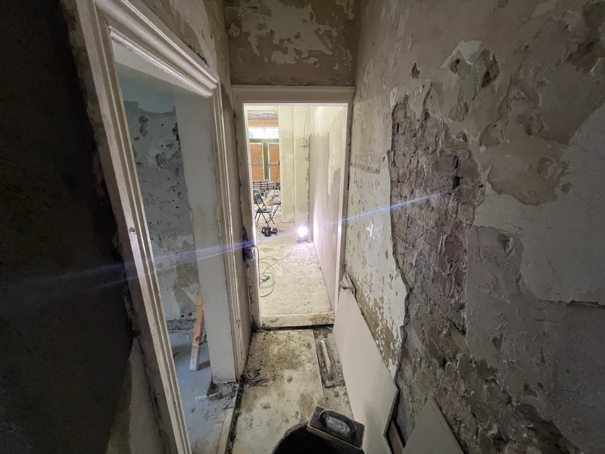 Inde i en renoveret lejlighed med skrald, tomme vægge og et gulv i underopførelse og en åben dør