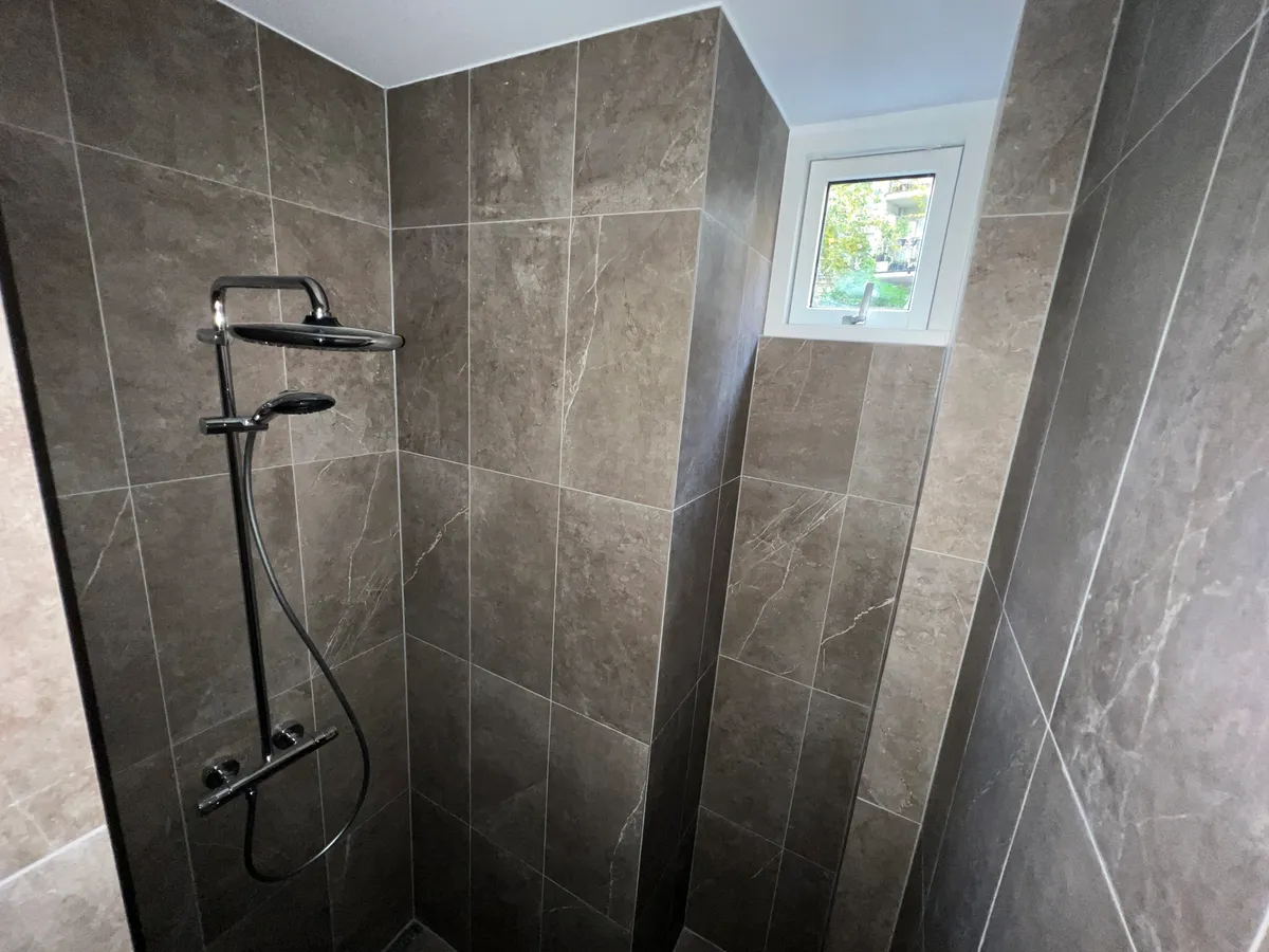 Moderne, luksuriøs grå marmor badeværelse med hjørnebruser og rektangulært vindue i loftet