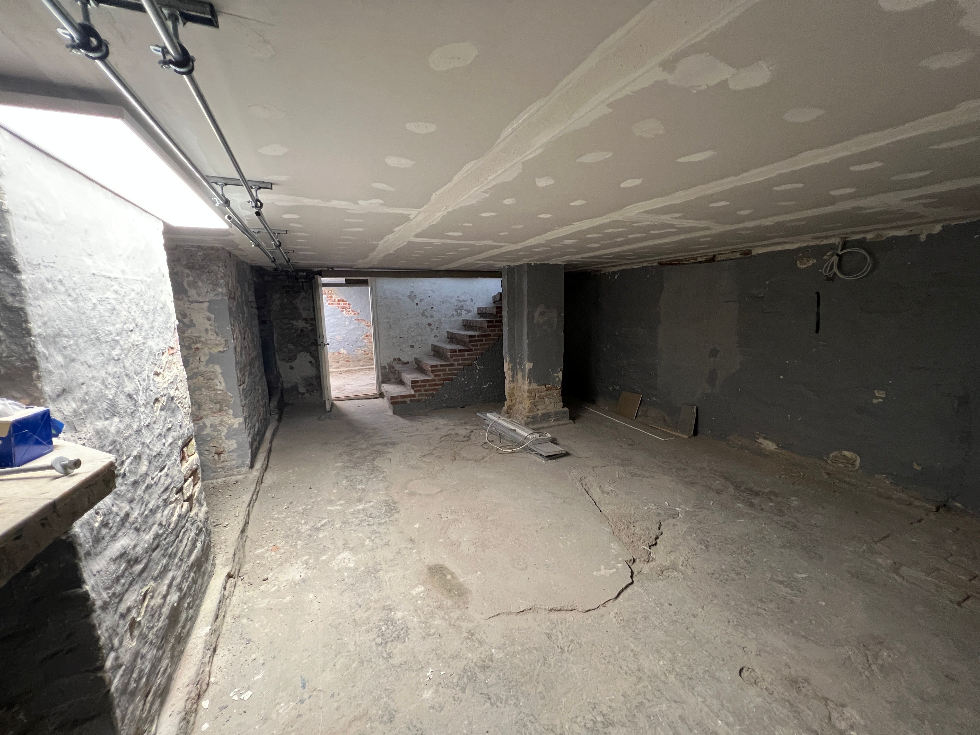 Under renovering i lysegang med skrappe vægge og loft med hvide prikker. Stykker træ og stål i loftet.