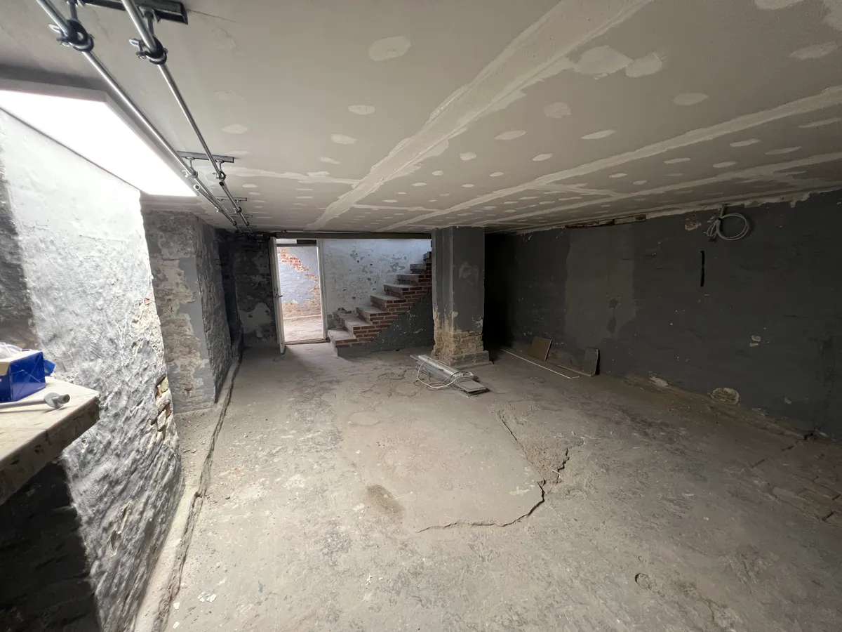 Under renovering i lysegang med skrappe vægge og loft med hvide prikker. Stykker træ og stål i loftet.