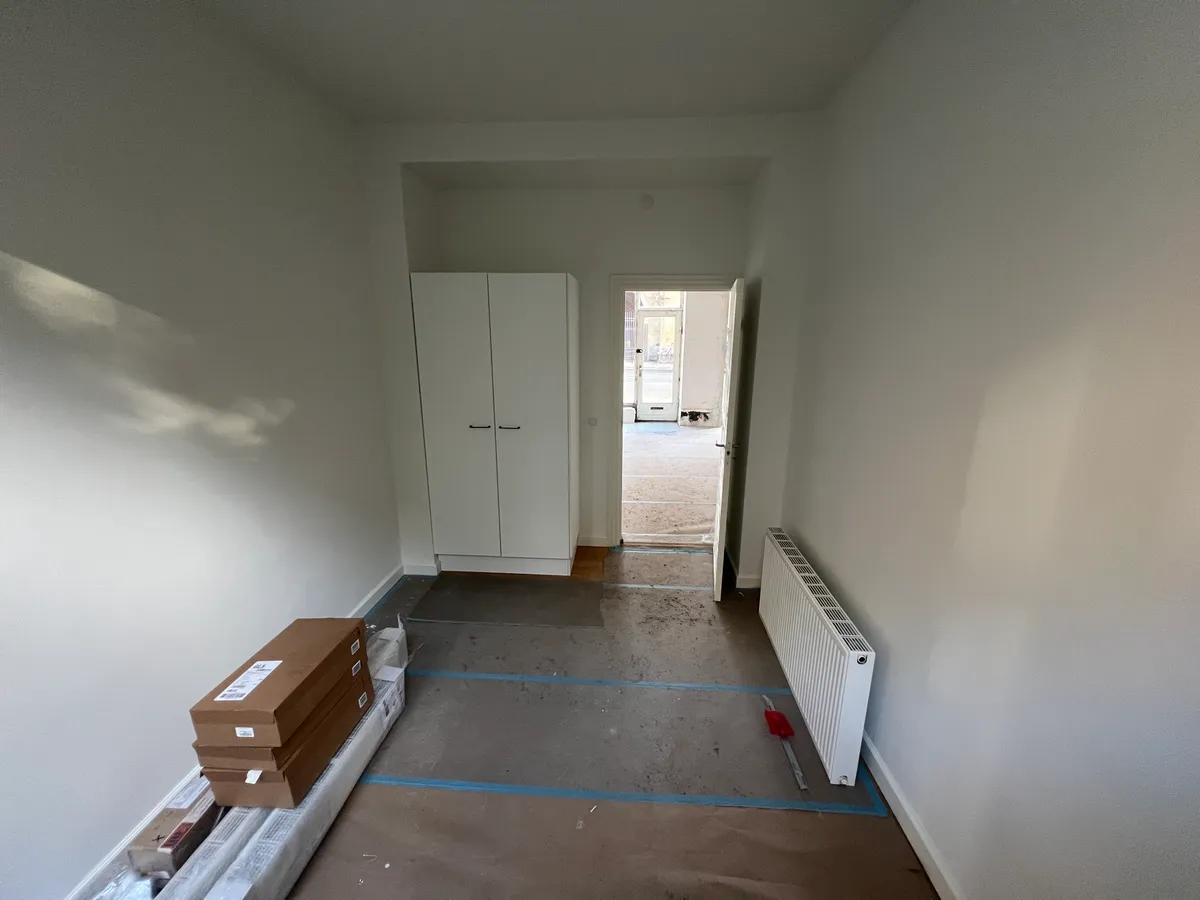 Nyrenoveret tomt rum med hvide vægge og gulvtæppe, og en hvid garderobe mod væggen, tomme bokse og en gulvmåler