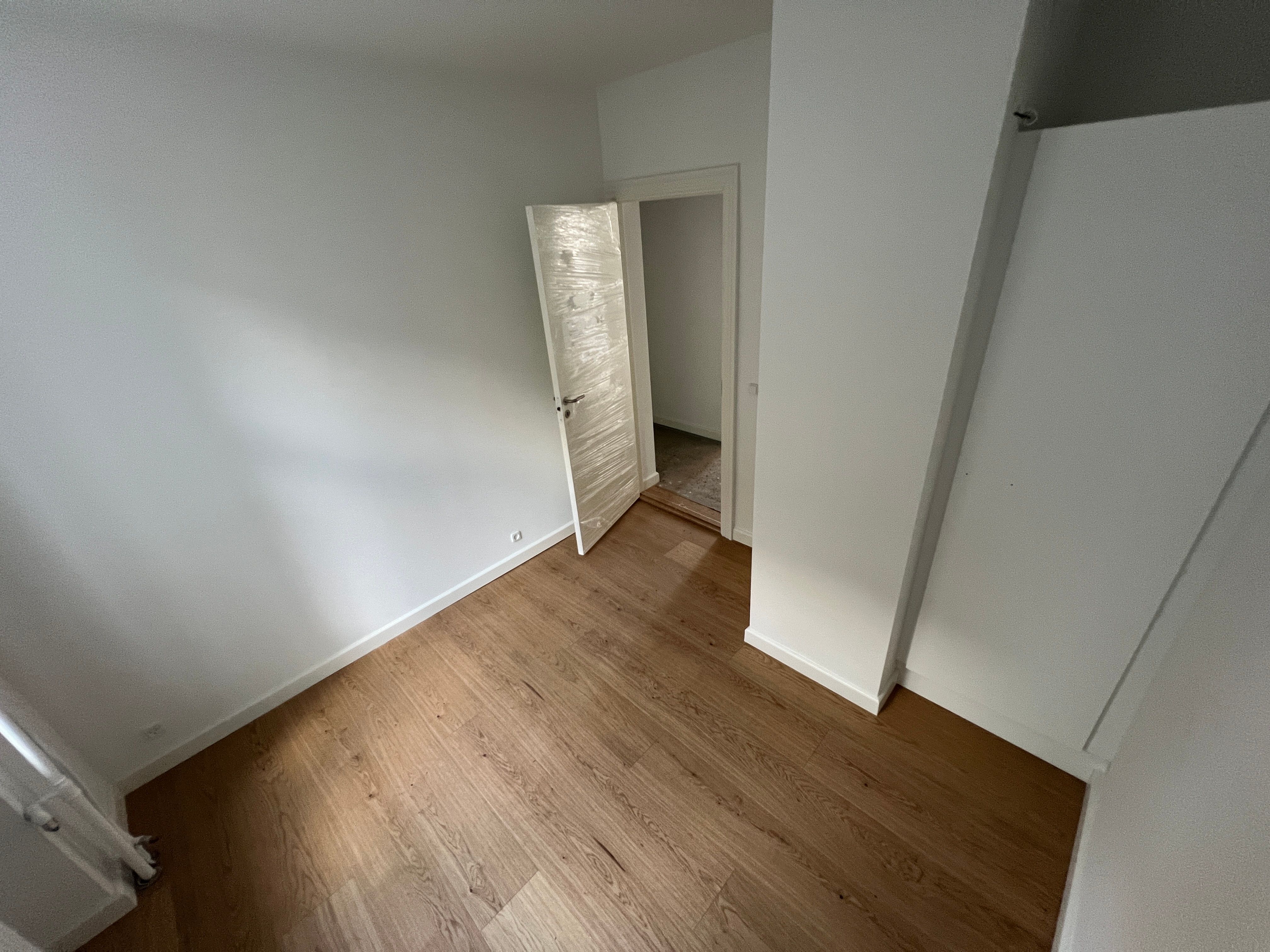 Moderne nyrenoveret lejlighed med åbne døre og parketgulv på gulvet. Væggene er hvide og en hvid dør er åben mod et tomt rum