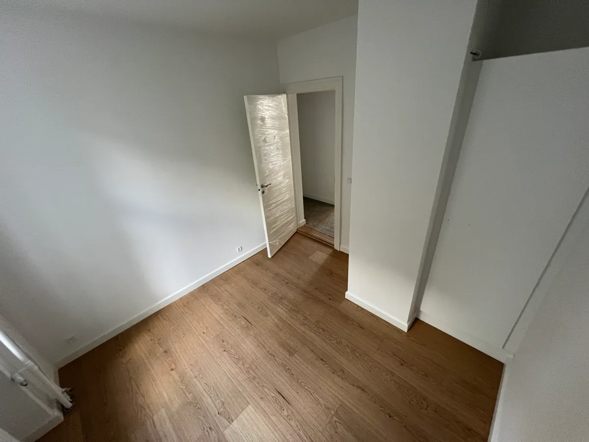 Moderne nyrenoveret lejlighed med åbne døre og parketgulv på gulvet. Væggene er hvide og en hvid dør er åben mod et tomt rum