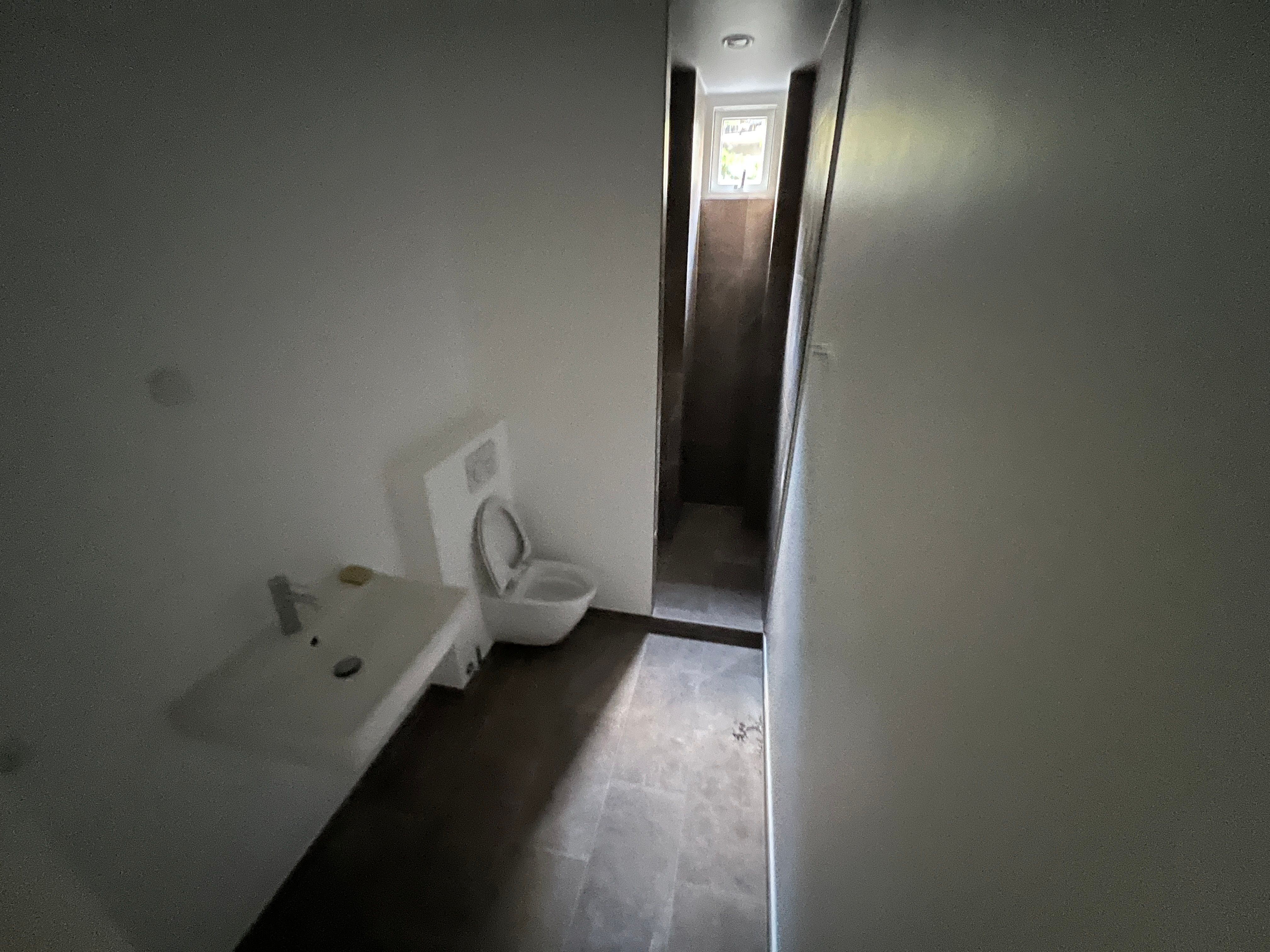 Toilet med hvidt toilet, hvidt vask og gulv med mørk belægning i en moderne og ren interiørdesign