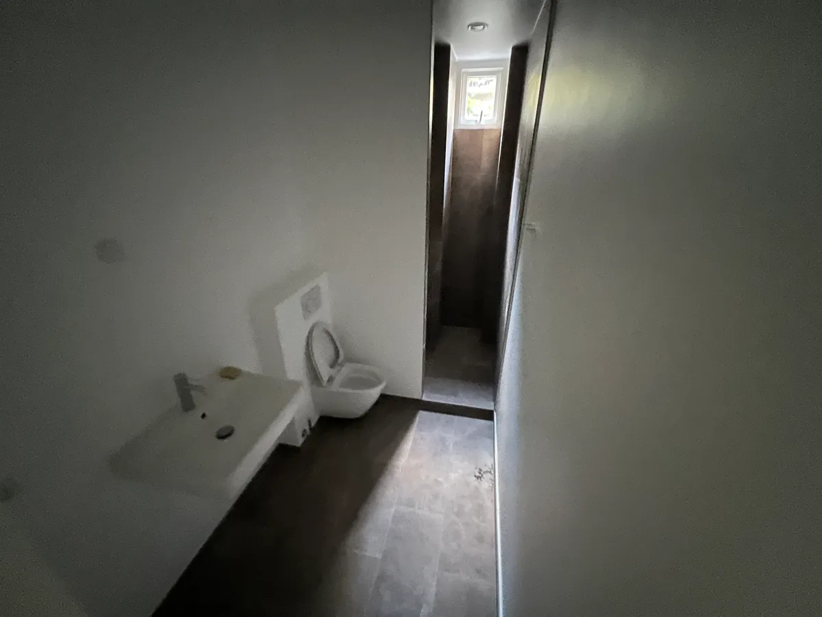 Toilet med hvidt toilet, hvidt vask og gulv med mørk belægning i en moderne og ren interiørdesign