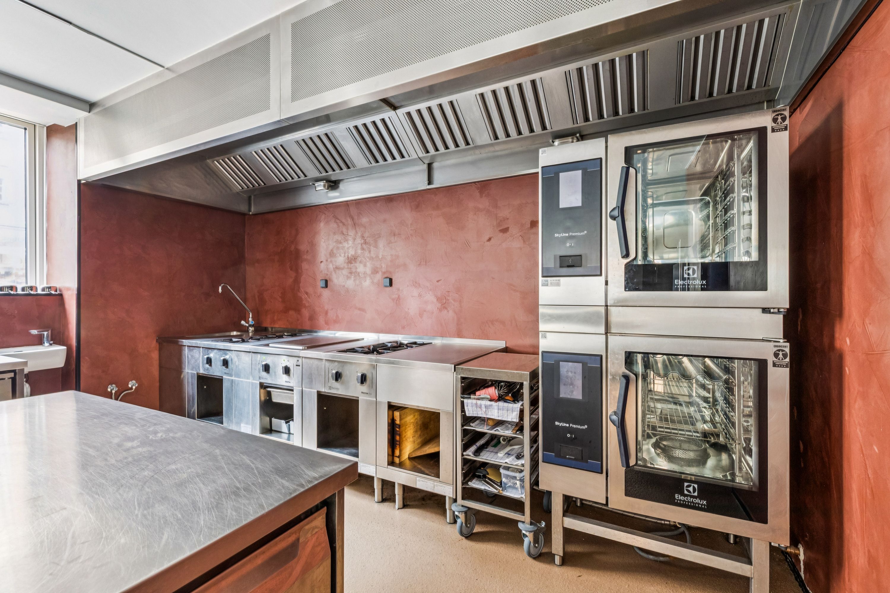 En moderne kommerciel køkken med elektriske komfurer, en stor industrikøleskab, og en professionel elektrisk ovn