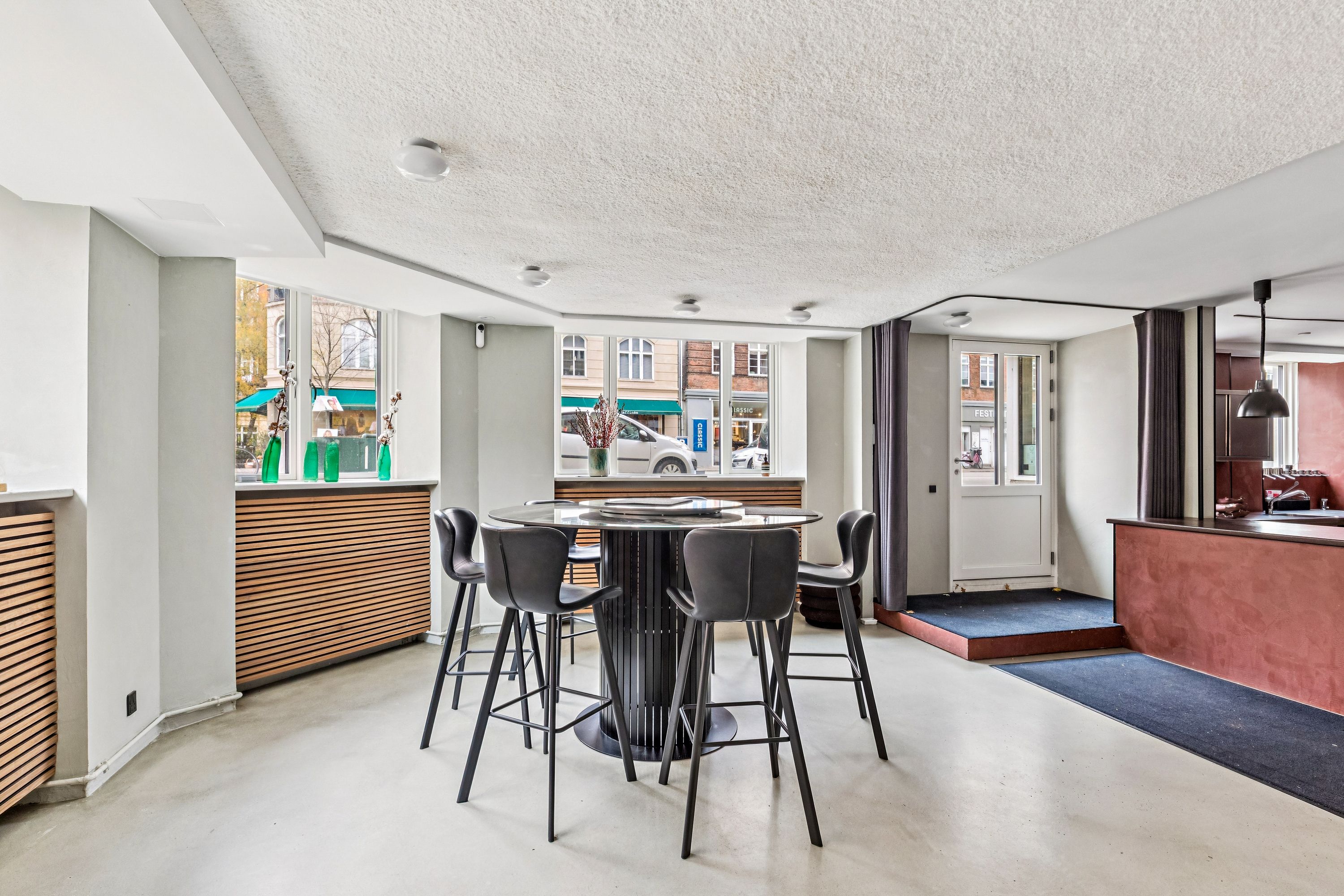 Moderne minimalistisk køkken med rundt glasbord og læderstole samt en udsigt til gade med biler og forretninger