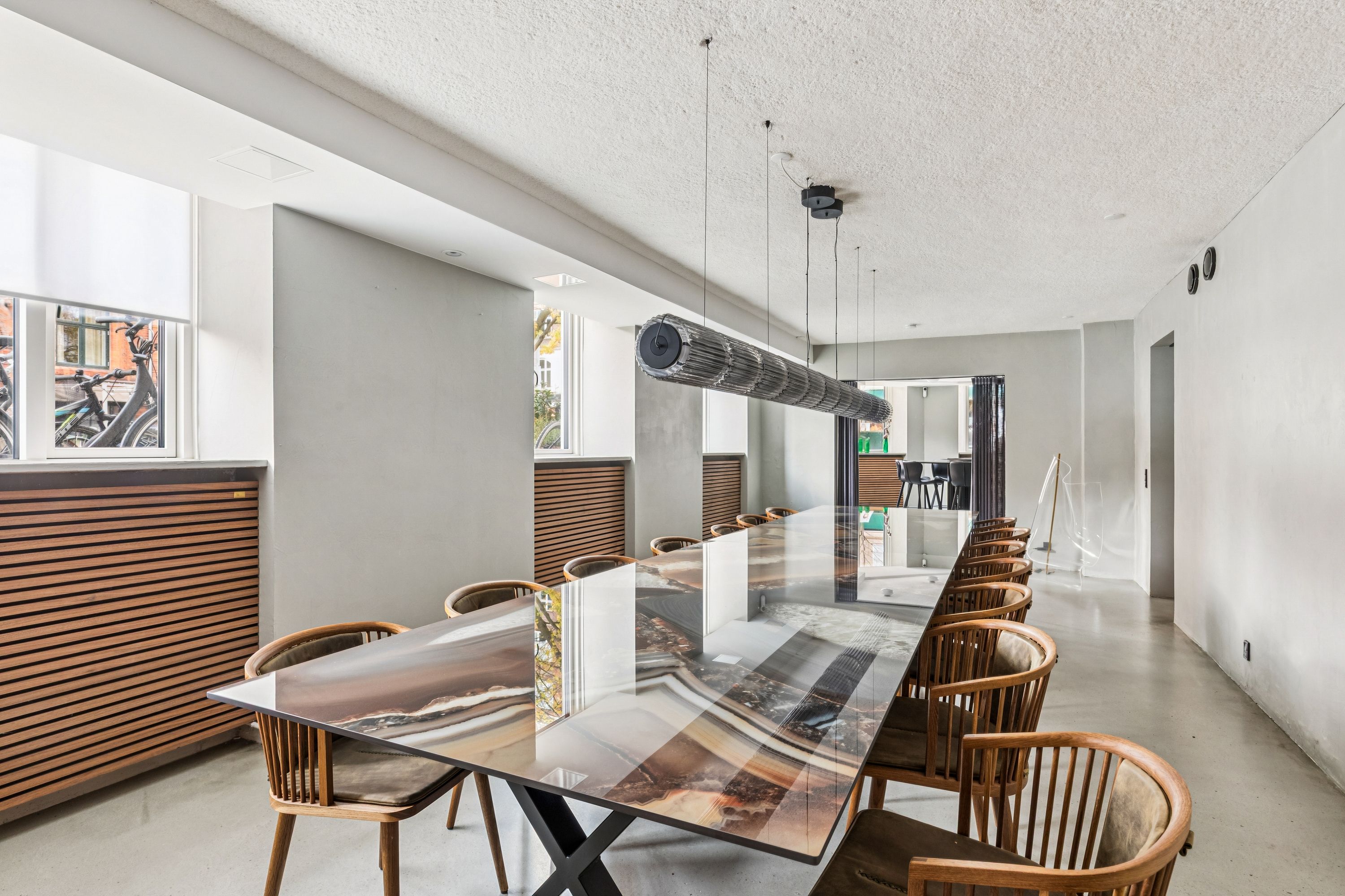 En lang glasbord med masser af stole og en lysekron over bordet i en moderne stil med hvide vægge og træindslag