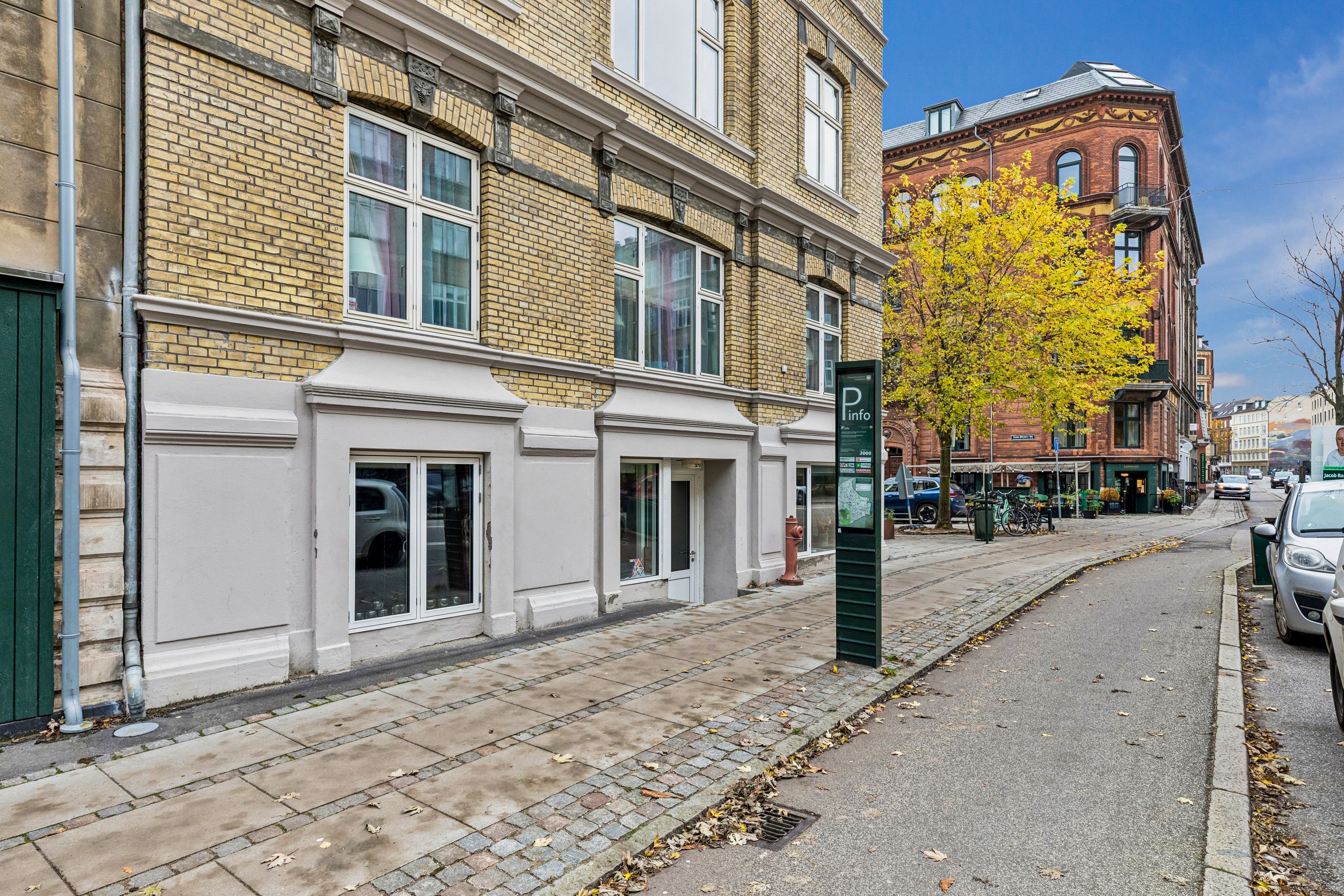 En bygning med gul puds og røde mursten i Frederiksberg, der står ved siden af en grøn buske, et rødt hydrant og en mappe