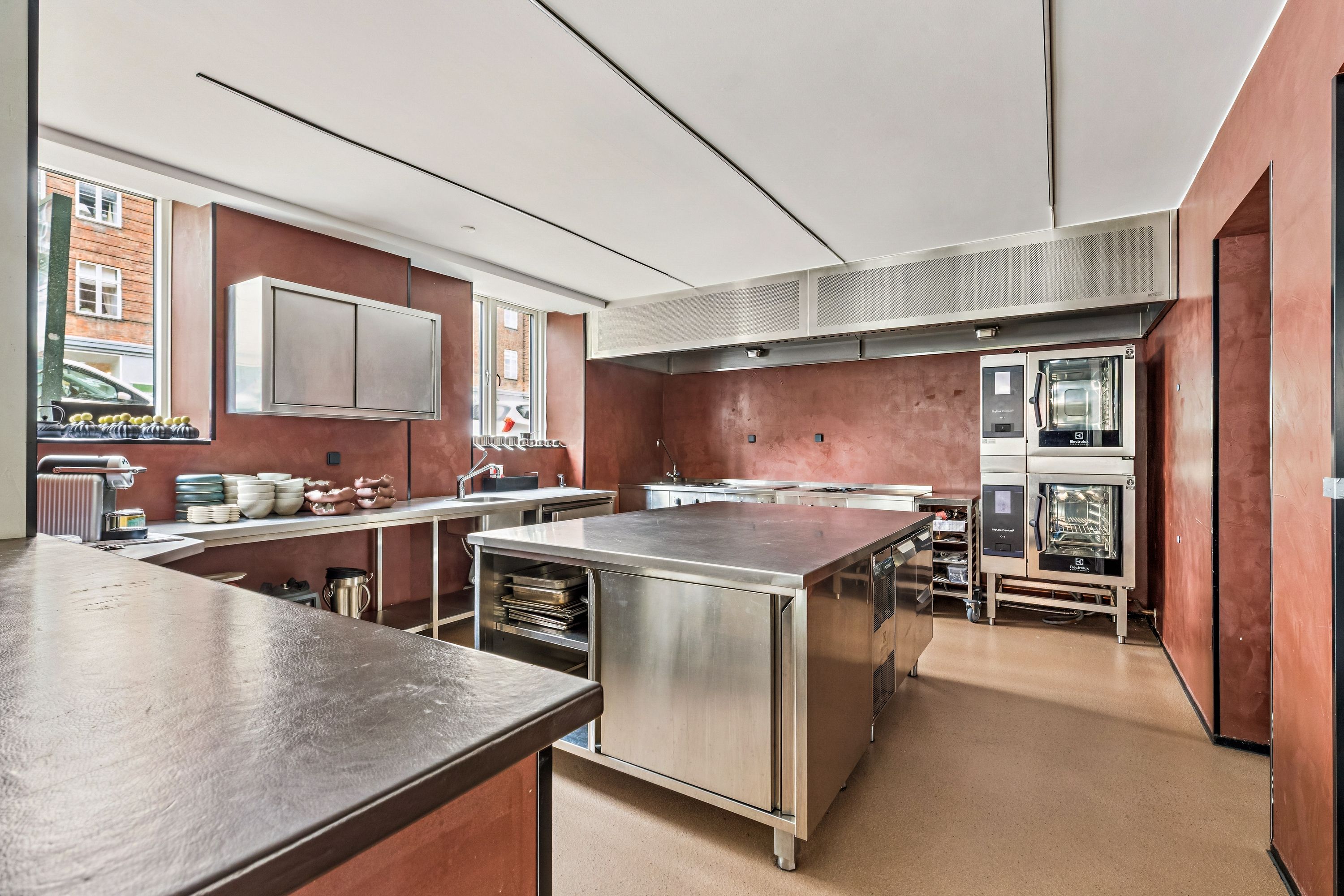 En moderne køkken med rustfrit stål og røde vægge samt to ovne og et værktøjsbord med kobbertop