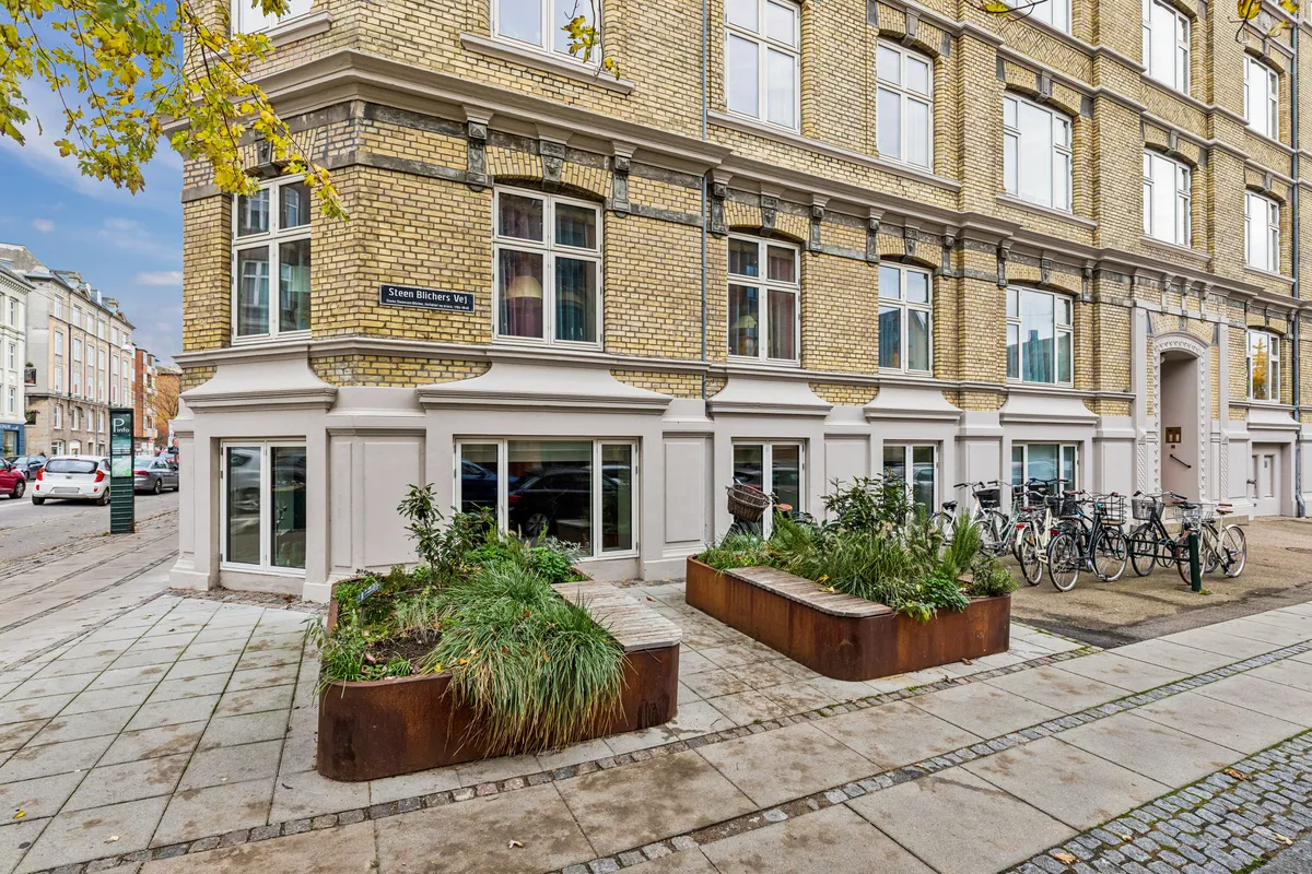 En bygning med flere lejligheder, store ruder og gårdhave med planter og cykler i nærheden