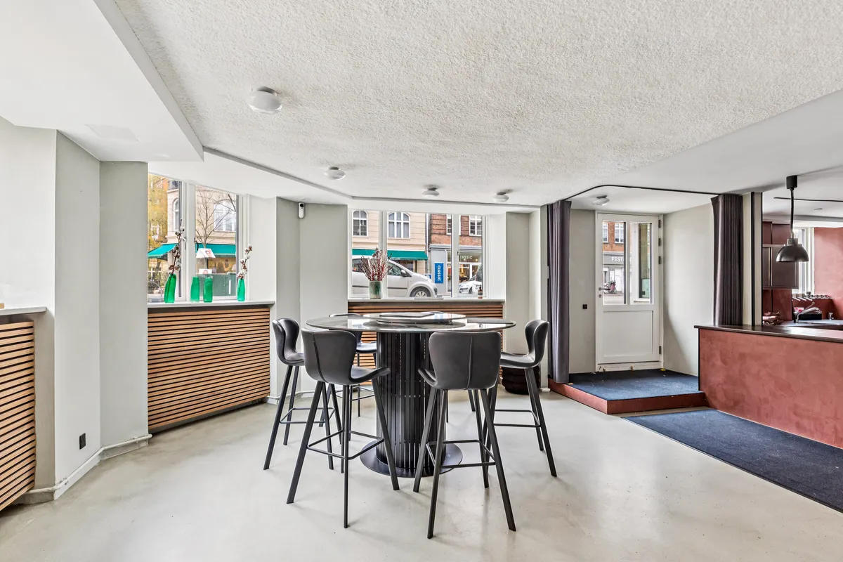 En moderne køkken med en rund spisestue og barstole samt store vinduer med udsigt til gaden og en blomsterudsmykning