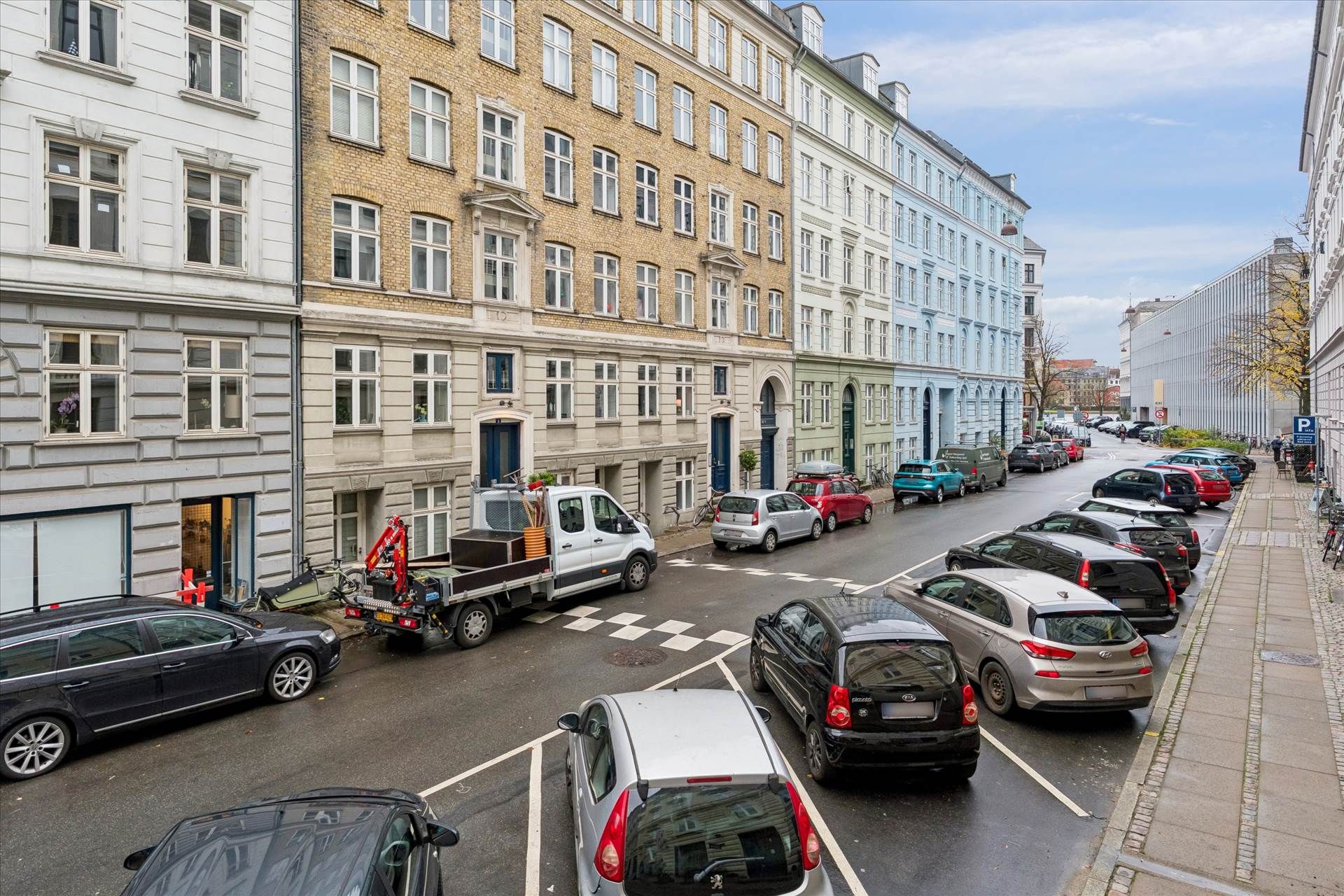 Parkerede biler på Turesensgade 11 og en tung lastbil med kran i forgrunden og flere bygninger i baggrunden