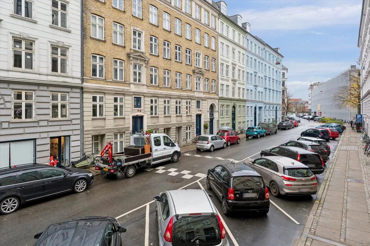 Parkerede biler på Turesensgade 11 og en tung lastbil med kran i forgrunden og flere bygninger i baggrunden