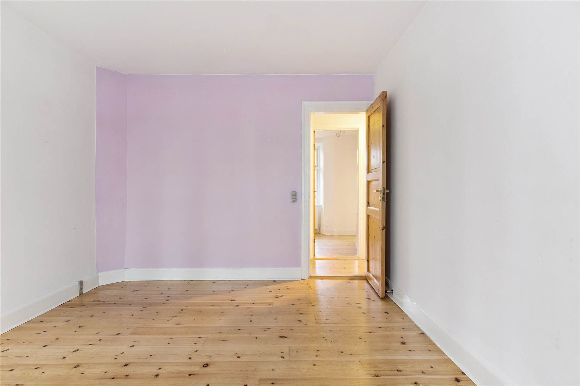 Køkken med køkkenhjørne og trægulv, hvor det ene væg er mallet i lyserødt og gulvet er lysebrunt