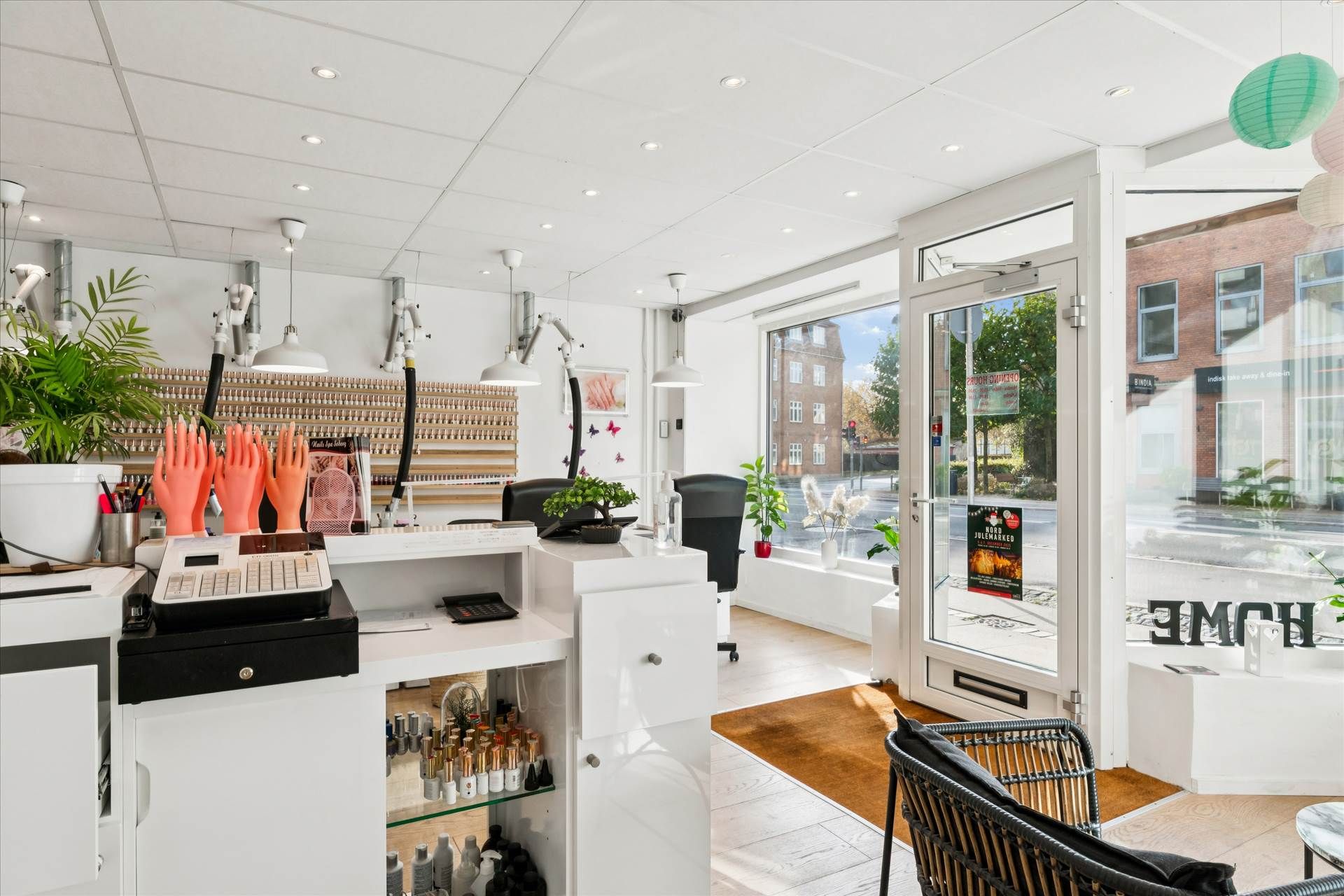 Hvid indretning med høj gulvbelægning og lysekroner med skumle lys. På højre side er en indgang med skrift og plante i